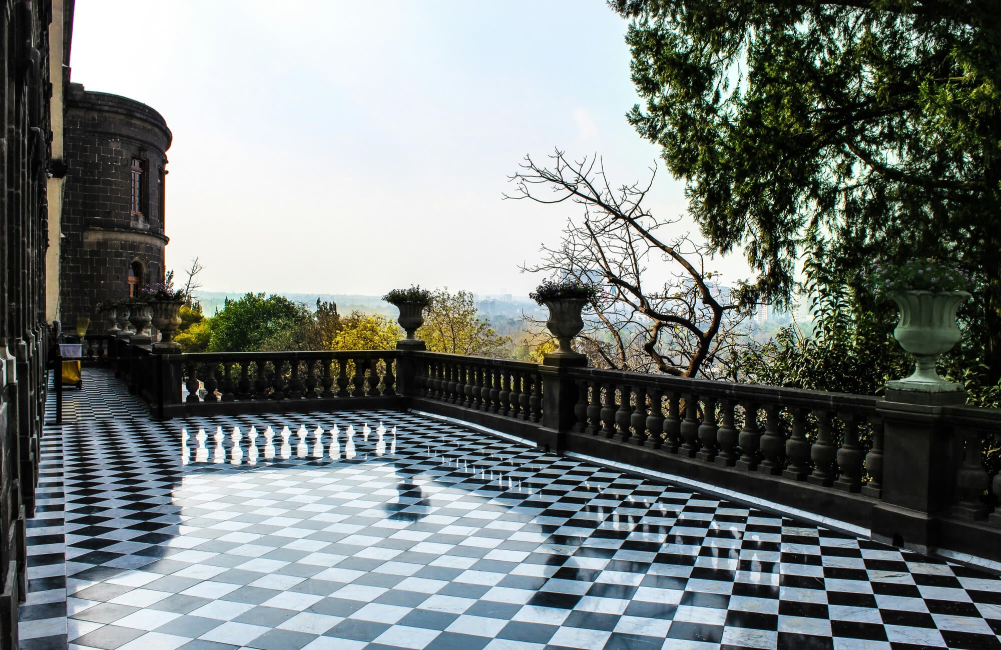 null Spacious terrace featuring a polished black and white checkered floor, framed by stone balustrades and lush greenery with a scenic view