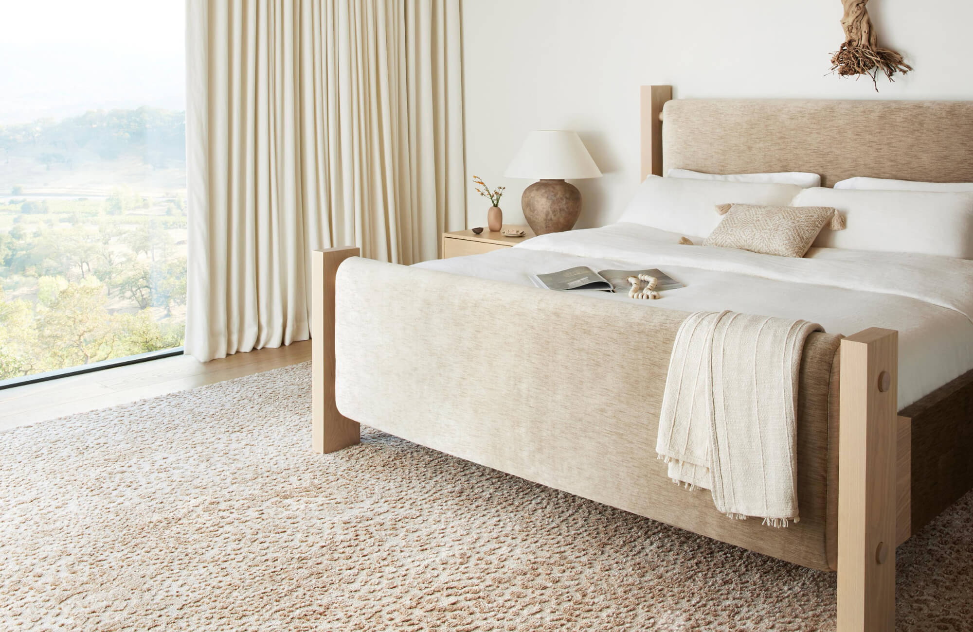 null Serene bedroom with a spacious neutral rug, upholstered bed, soft linens, and floor-to-ceiling curtains framing a peaceful outdoor view.