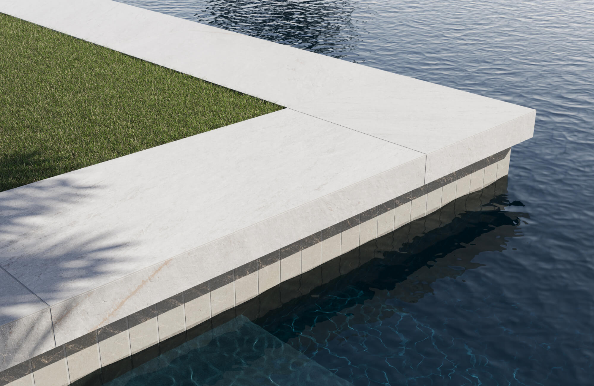null Refined pool coping with light porcelain stone tiles and dark accent trim, framing lush green grass and deep blue water.