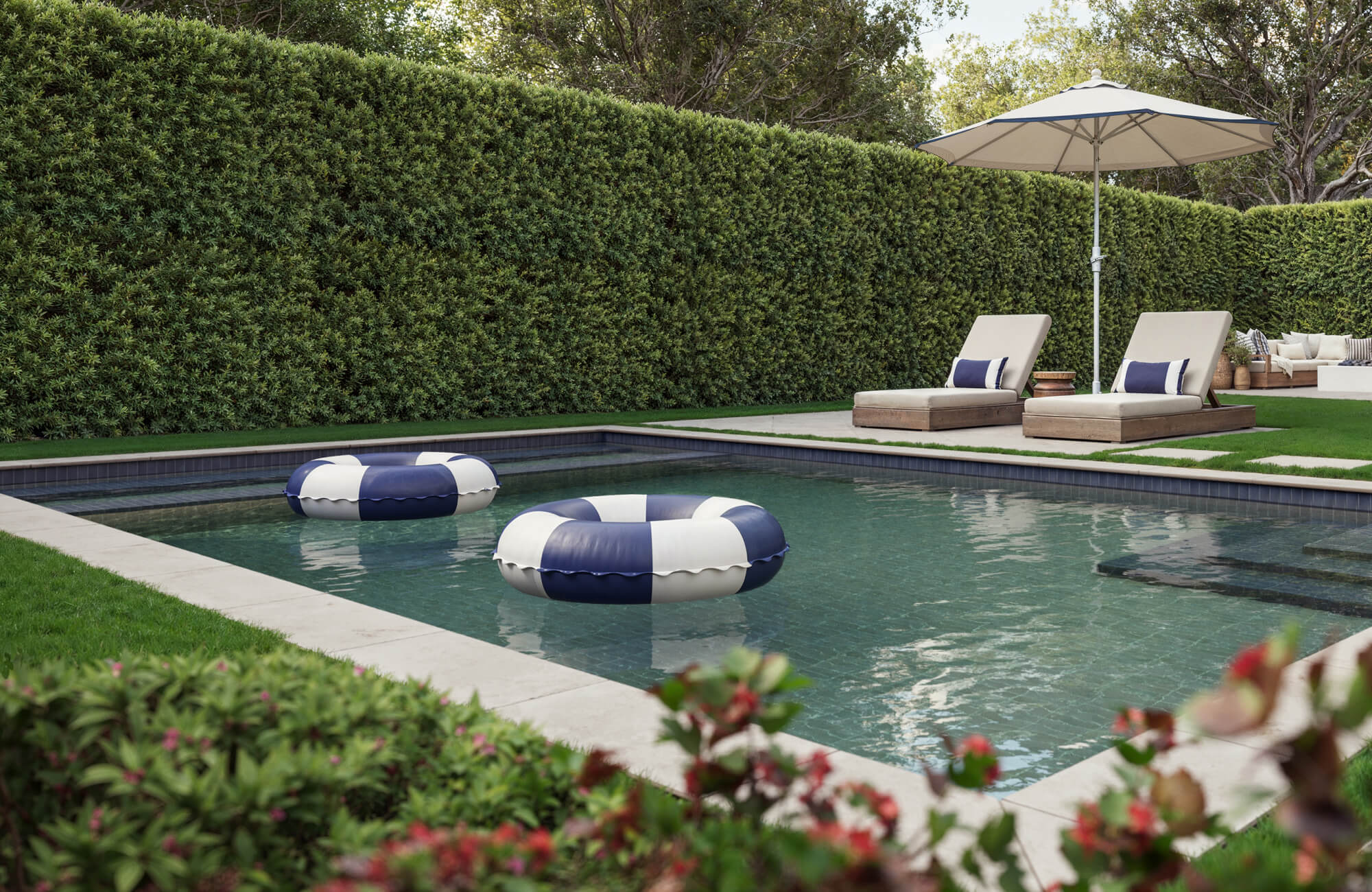 null Tranquil backyard pool with porcelain charcoal-toned tiles, framed by lush hedges, sleek stone pavers, and cozy loungers.