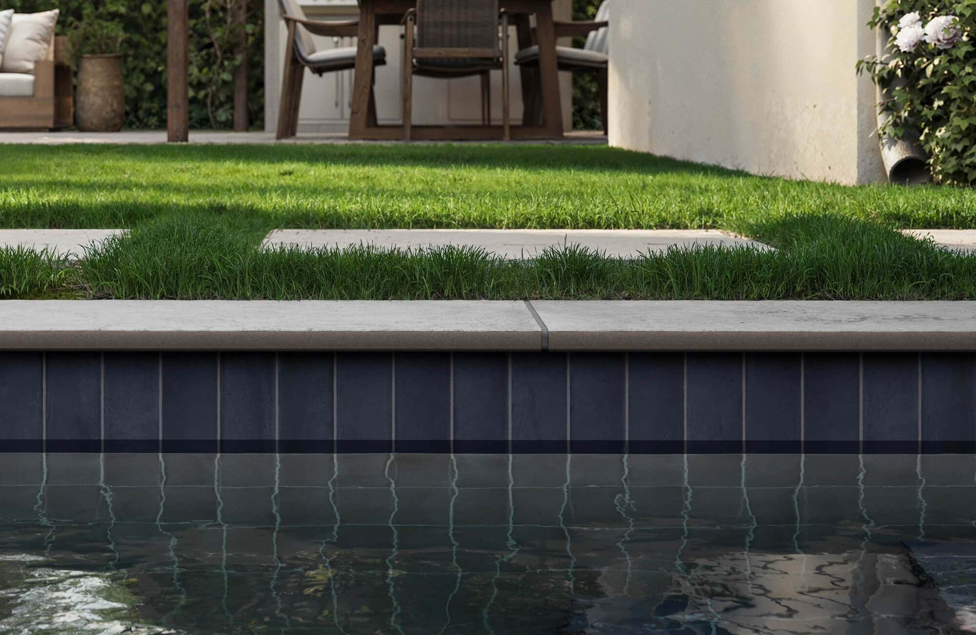 null Sleek dark porcelain pool tiles with subtle gloss, bordered by clean concrete coping and surrounded by lush modern landscaping.