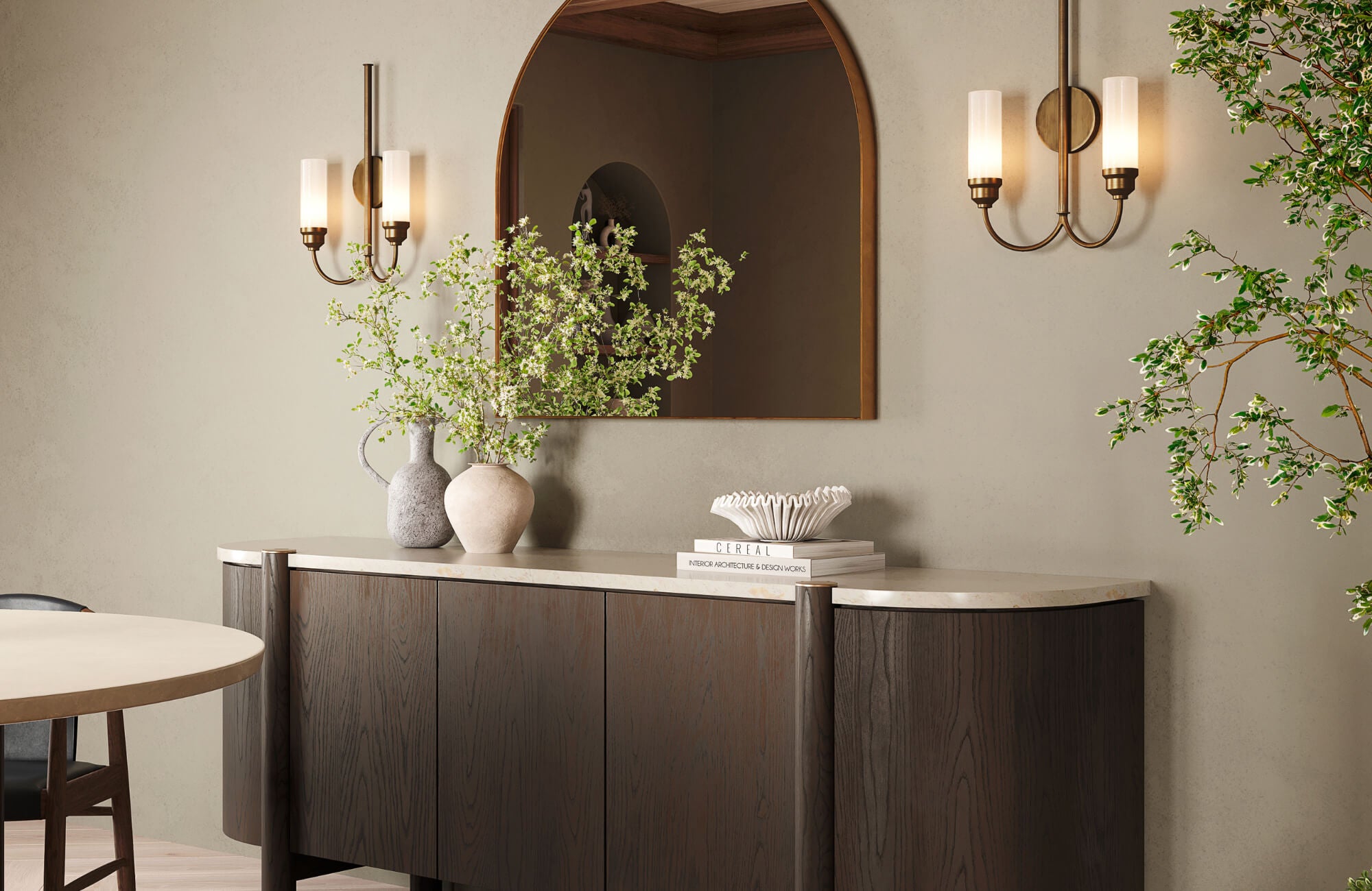 Arched mirror above a dark wood sideboard with sculptural decor and wall sconces in a refined, minimalist space.