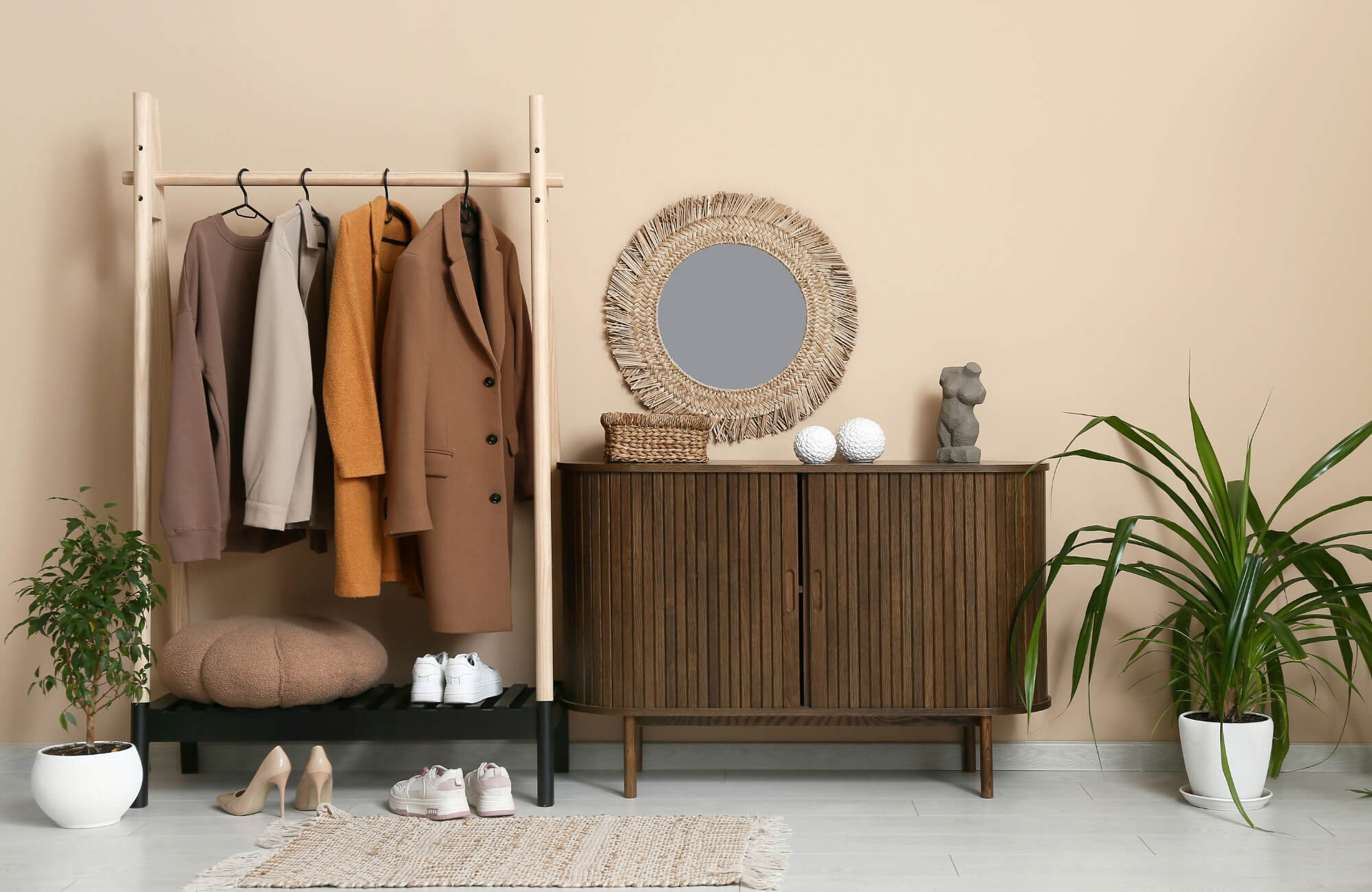Entryway with a dark wood sideboard, woven round mirror, coat rack, plants, and neutral-toned accessories.