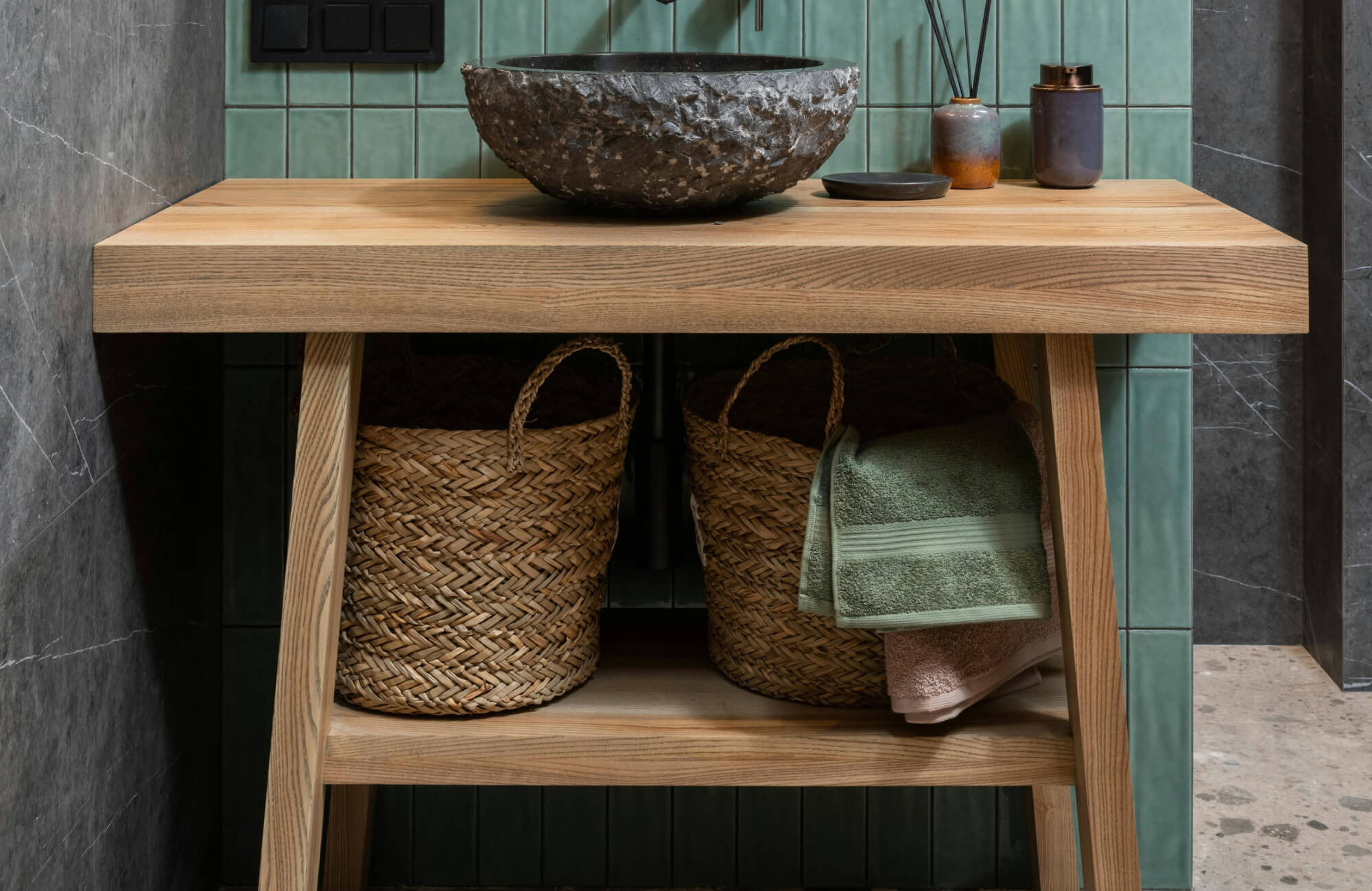 Rustic bathroom vanity with a natural wood countertop, stone vessel sink, and warm ambient lighting that highlights the textured green tile backsplash.