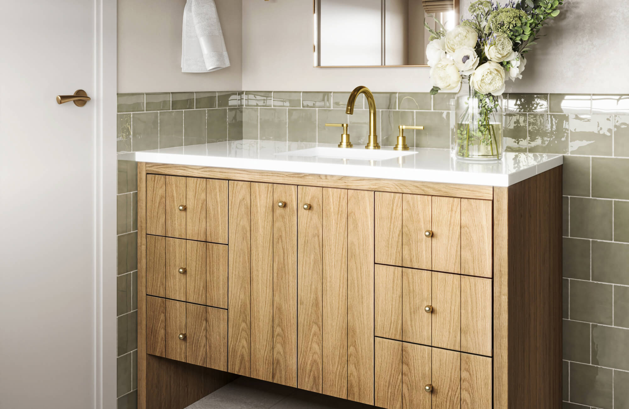 Modern bathroom vanity with a natural wood cabinet, white countertop, and brass fixtures, accented by soft green tile backsplash and fresh floral décor.
