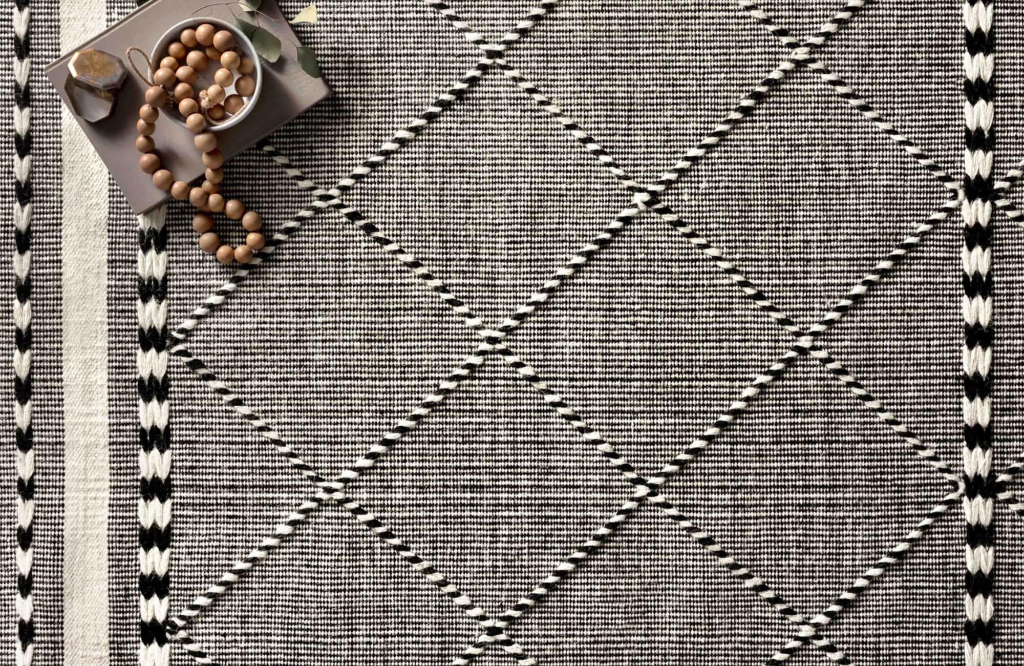 Close-up of a black and white Moroccan rug with diamond patterns, featuring a small bowl of wooden beads and decorative stones.