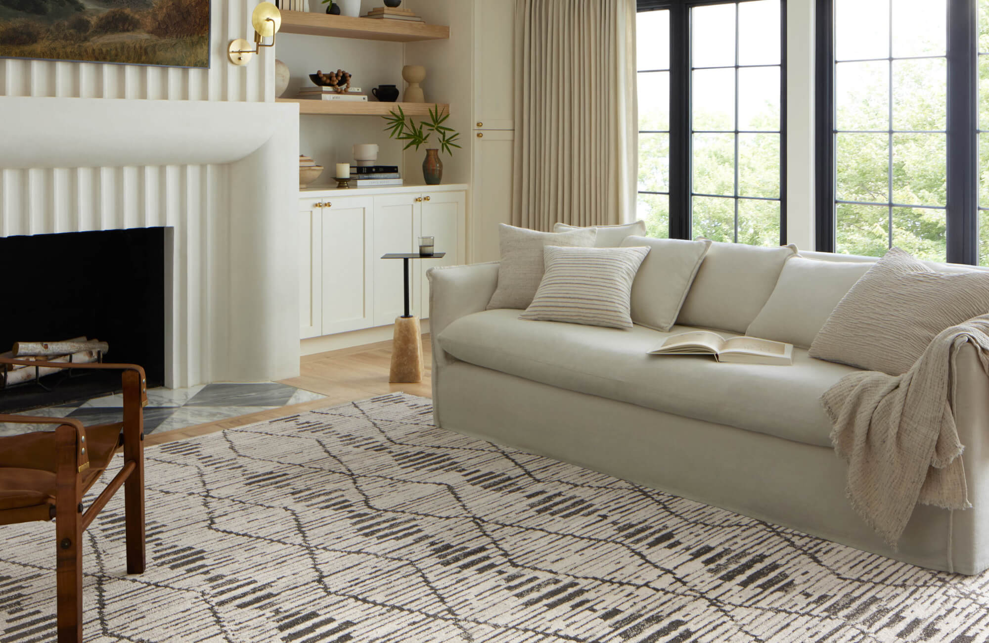 Elegant living room with a light sofa, patterned Moroccan rug, modern fireplace, and large windows bringing in natural light.