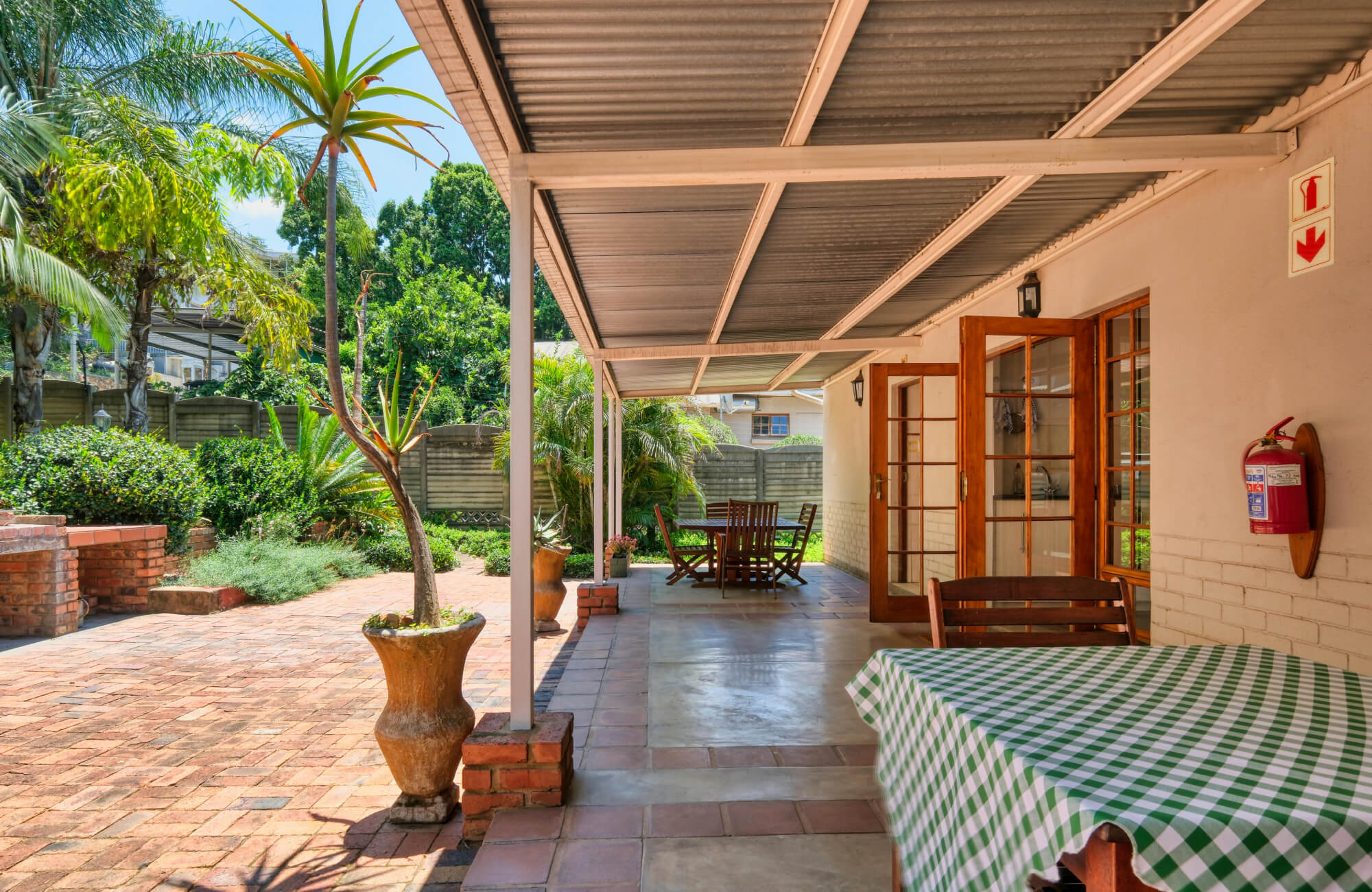 Spacious patio with terracotta brick flooring, shaded seating area, and potted plants beside wood-framed glass doors.