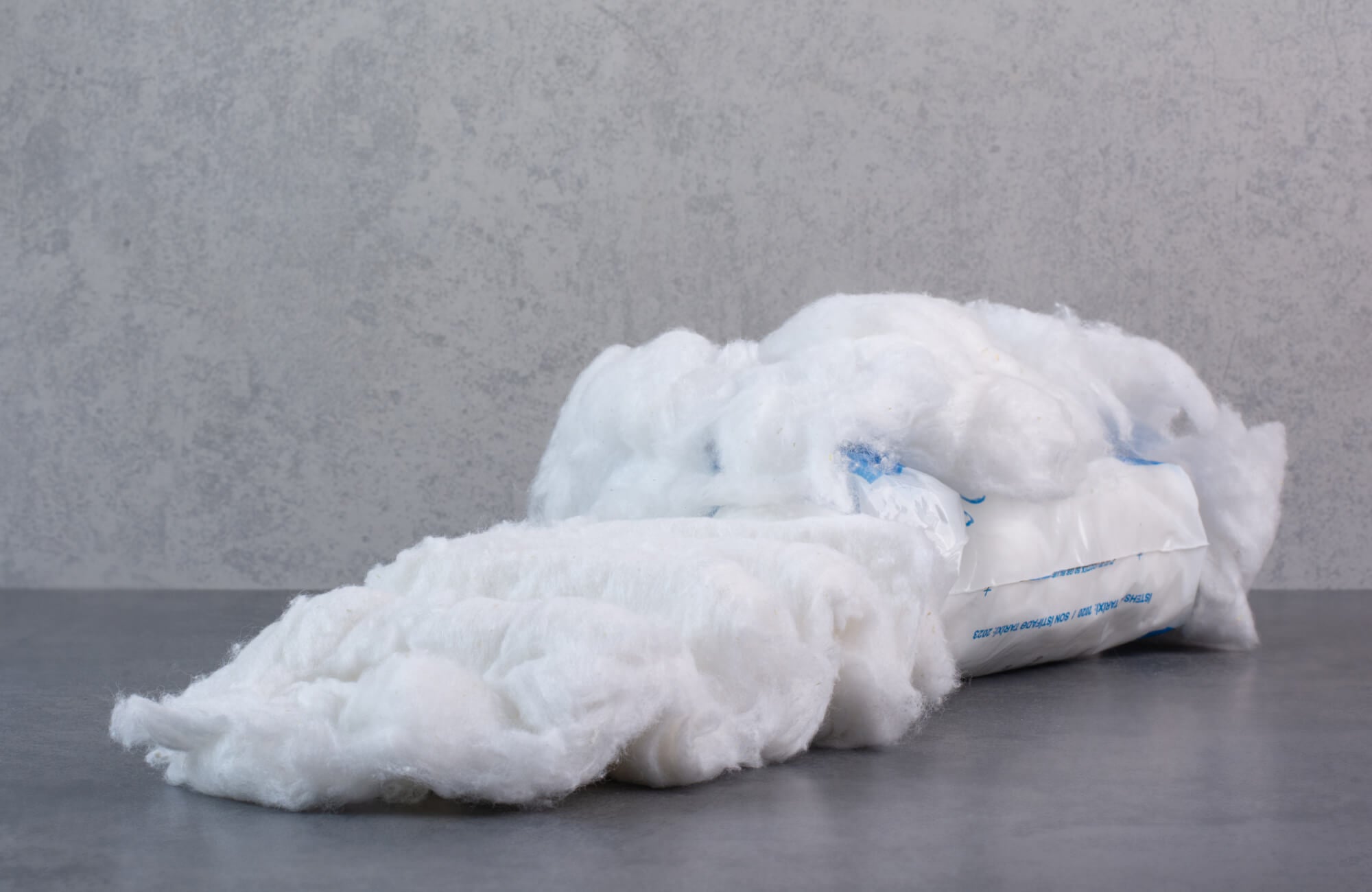 Close-up of white synthetic pillow stuffing with airy loft and lightweight structure on a gray surface.