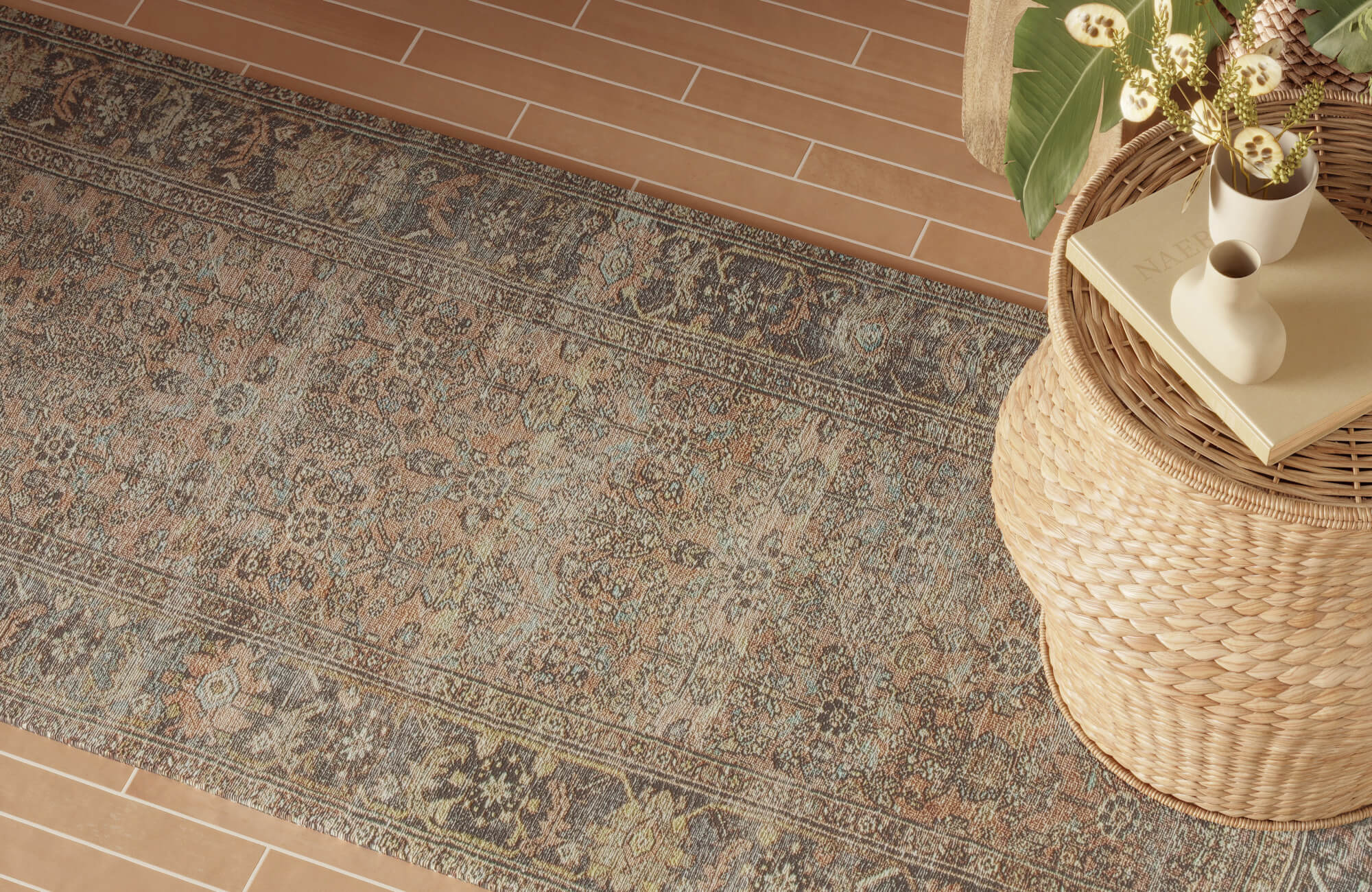 null Earth-toned patterned outdoor rug layered over terracotta plank tile, accented with a rattan drum table and neutral decor.