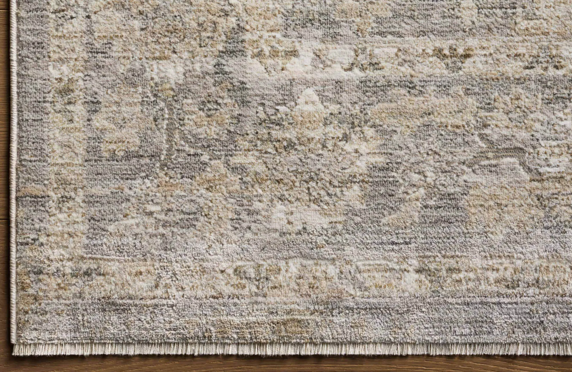Textured area rug in muted beige, cream, and grey tones with a distressed, vintage-style pattern and subtle fringe edge.