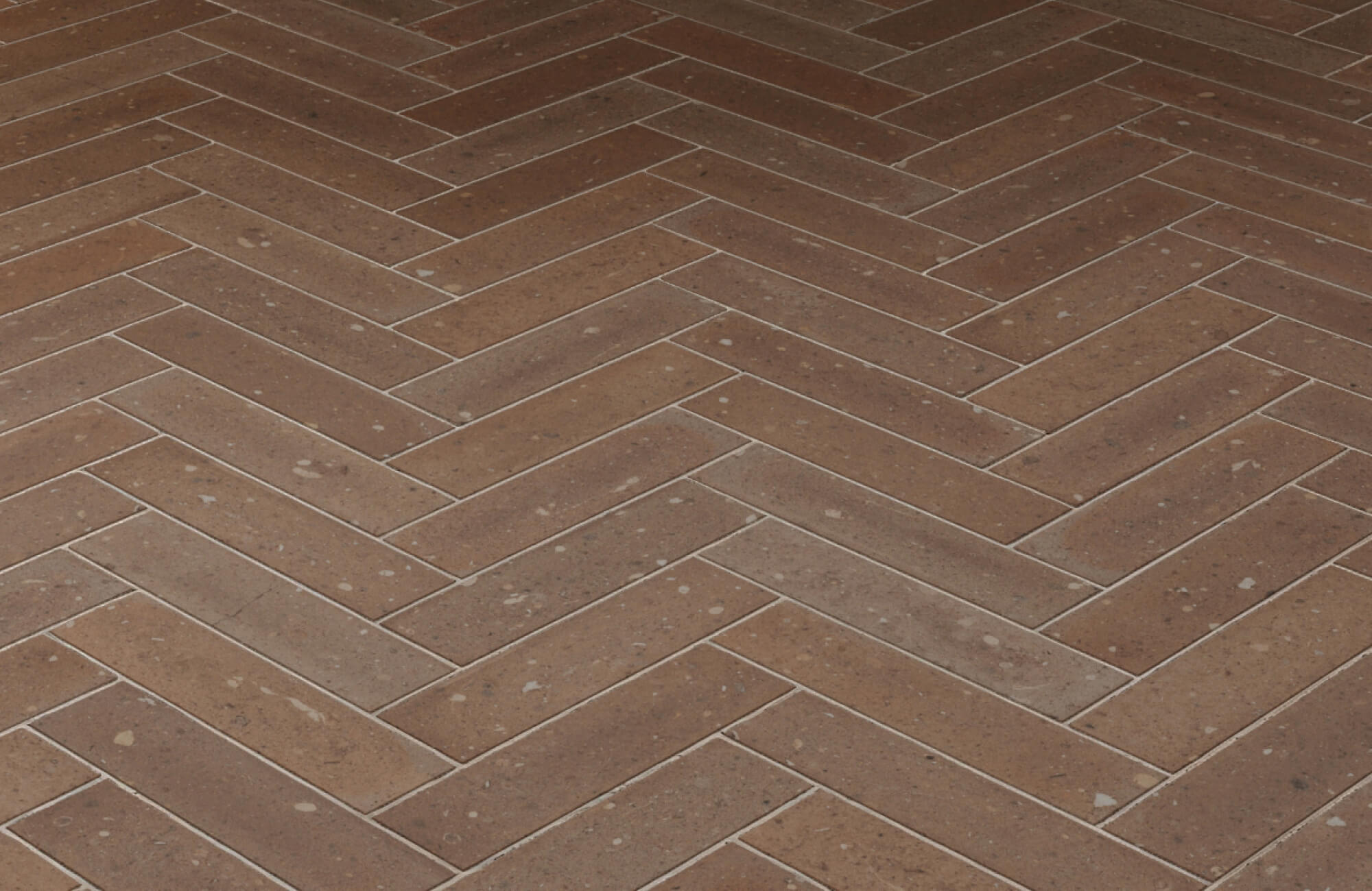 Ceramic terracotta-toned tiles in a classic herringbone pattern with subtle speckling for added texture and visual depth.