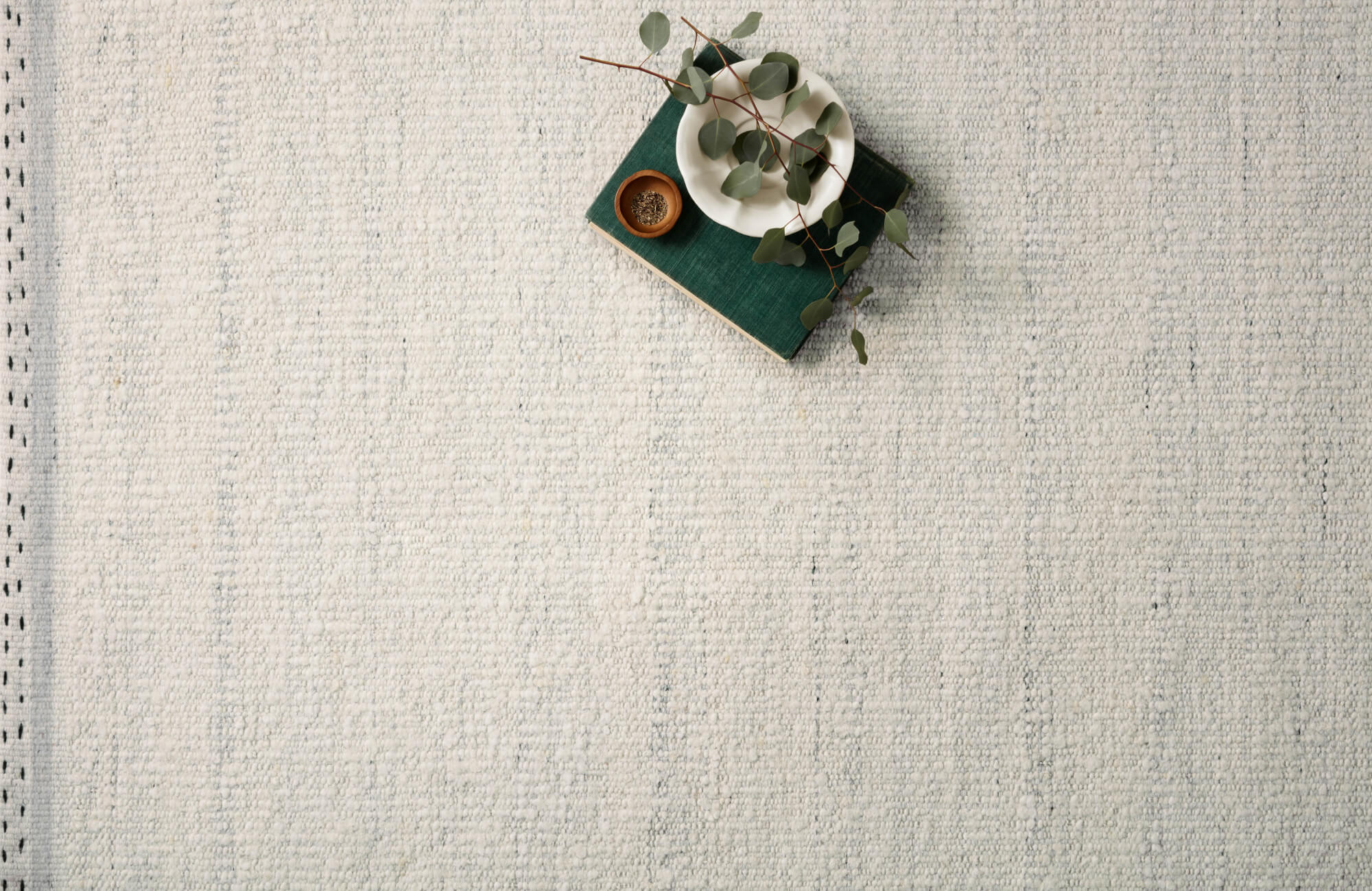 null Lightly textured ivory rug with subtle woven detailing, styled with a book, ceramics, and eucalyptus sprig.