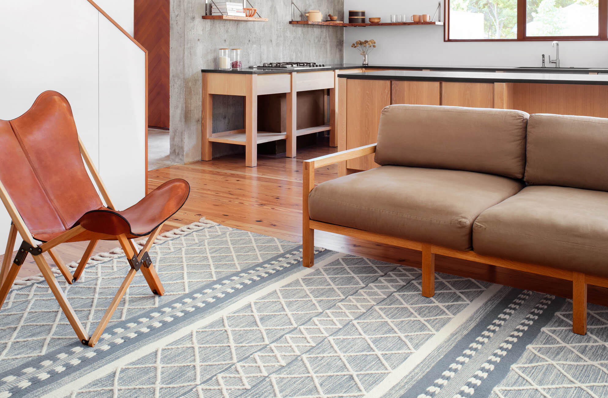 null Contemporary space with a geometric blue-and-ivory rug, tan leather chair, and wood-frame taupe sofa.