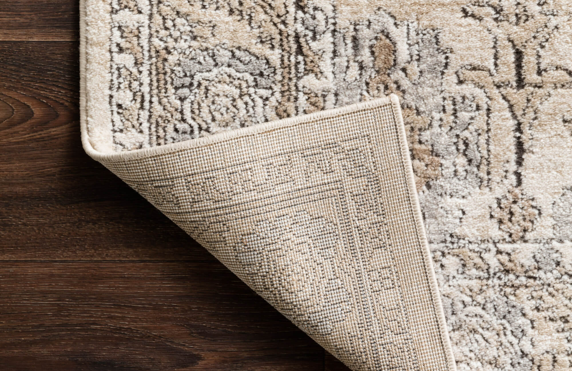 Detailed shot of a traditional-style rug in soft neutrals with the underside exposed, revealing a tightly woven synthetic backing.