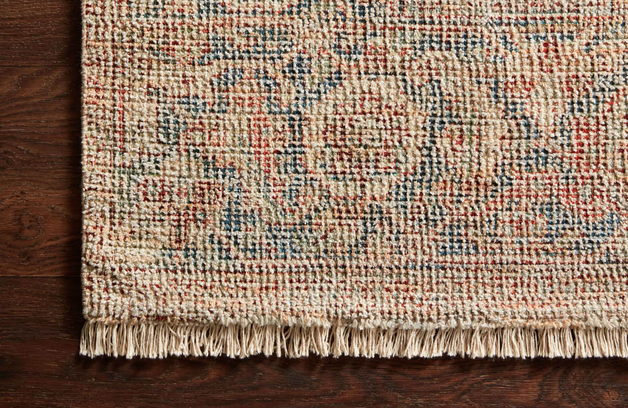 Close-up of a flatweave rug with multicolor pattern in red, blue, and beige tones, finished with short fringe along one edge.