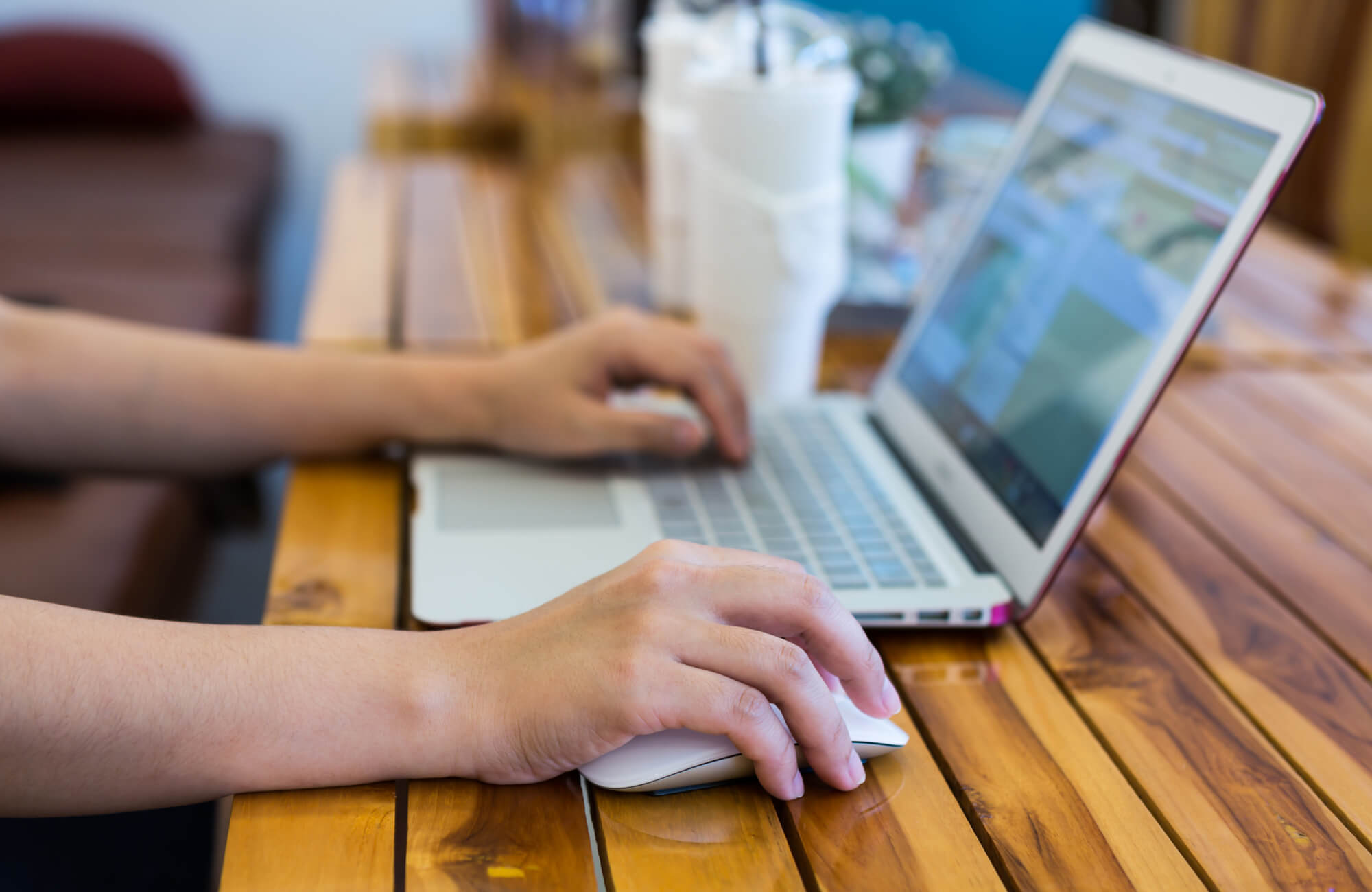 null Close-up of hands using a laptop and wireless mouse on a glossy wooden table, suggesting online browsing or shopping.