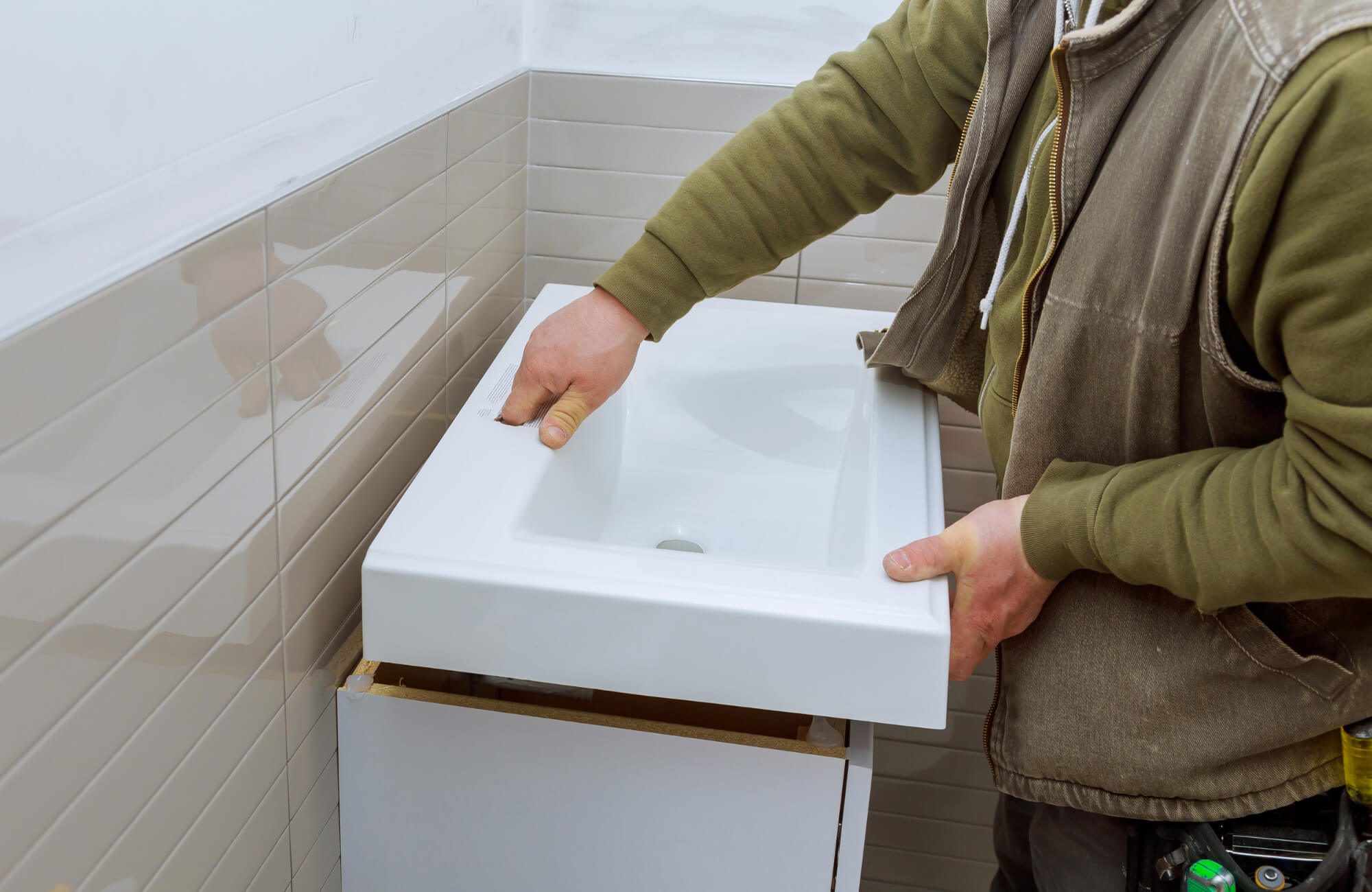 Worker installing a white ceramic sink on a bathroom vanity cabinet, aligning the fixture during plumbing and setup.
