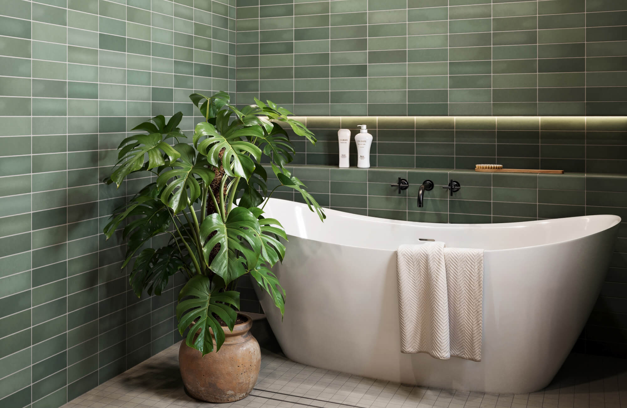 Serene bathroom with deep green subway tiles, a sleek freestanding tub, black fixtures, and a lush monstera plant in a terracotta pot.