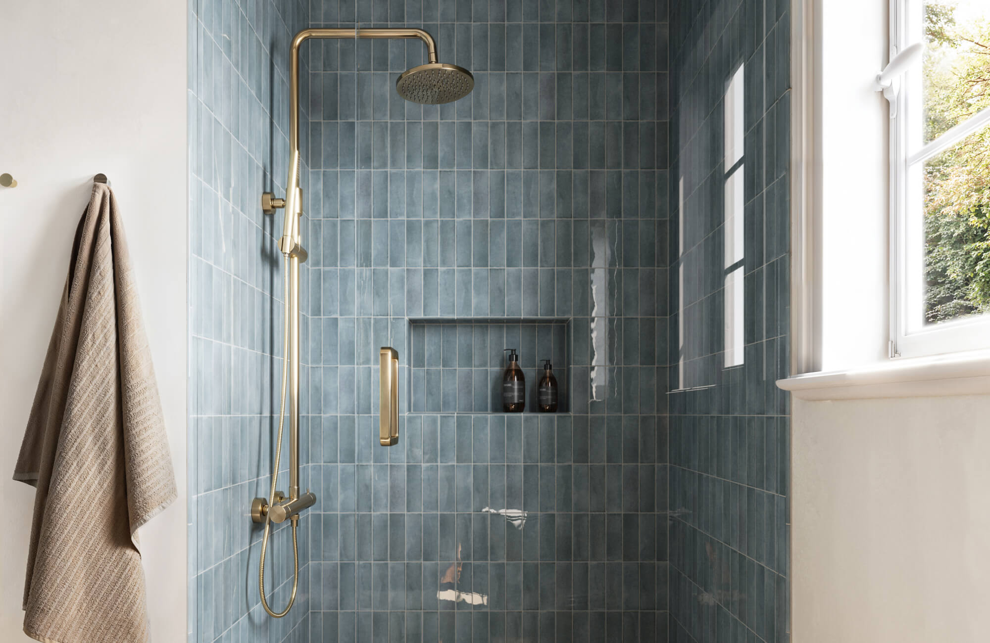 null A serene shower space featuring glossy blue-green subway tiles, a built-in niche and elegant brushed gold fixtures.
