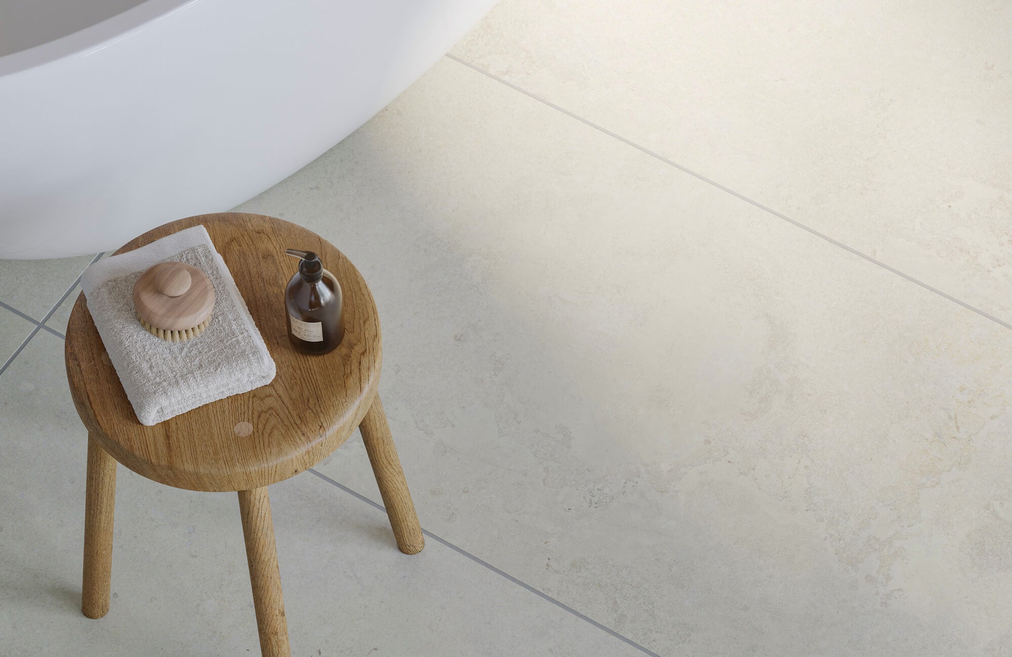 Close-up of beige stone-look bathroom floor tiles with subtle texture, gray grout lines, and wood bath stool.