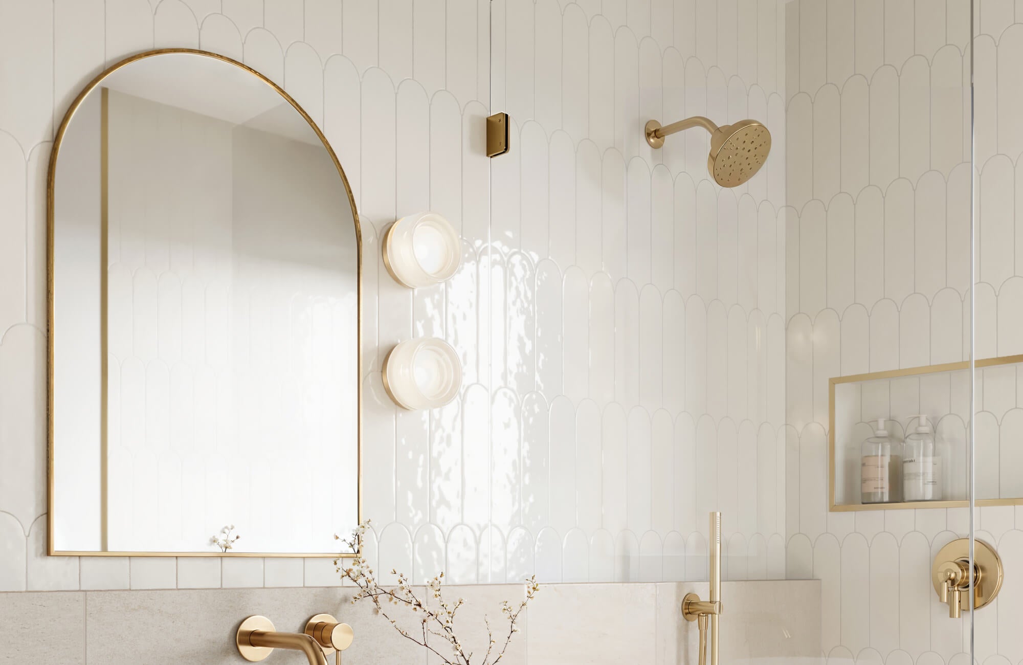 Elegant bathroom featuring glossy white scalloped tiles, brass fixtures, and an arched mirror, creating a bright and luxurious ambiance.