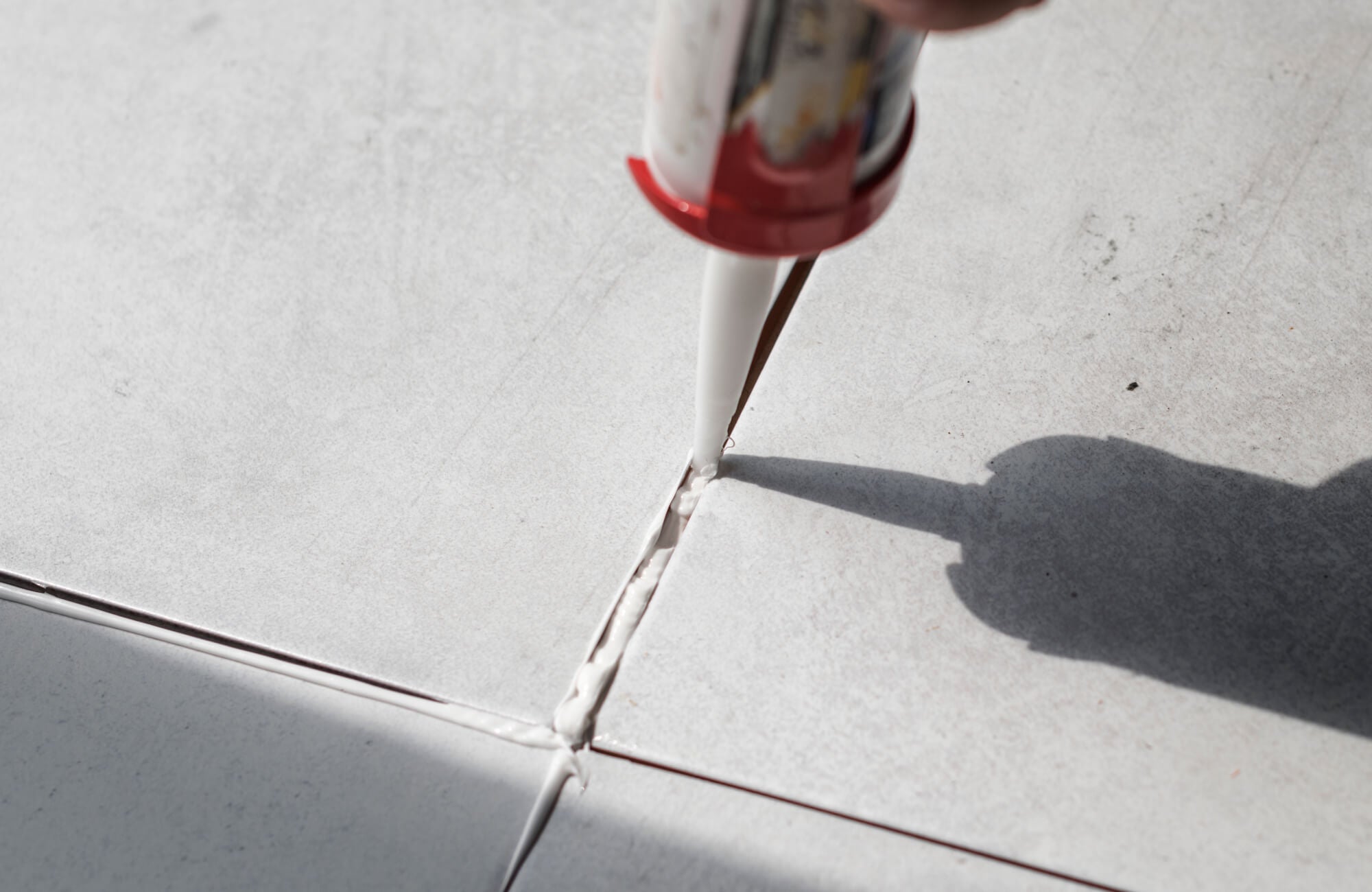 null Close-up of grout being precisely applied between light grey swimming pool tiles using a caulking gun for a seamless finish.