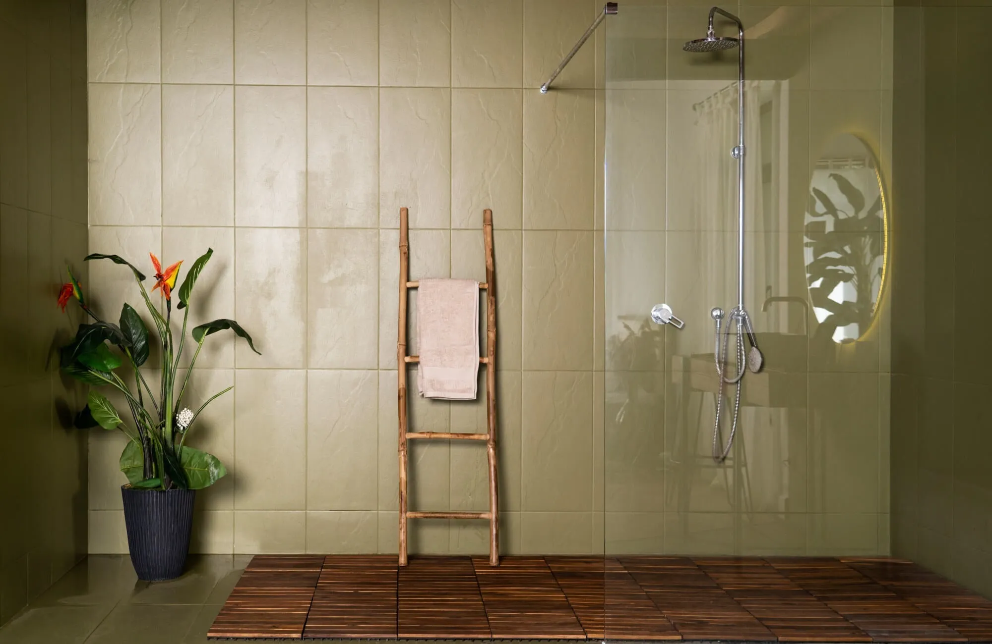Spa-inspired shower with large matte olive green wall tiles, wood flooring, a rainfall showerhead, and warm wood accents, creating a serene, nature-inspired retreat.