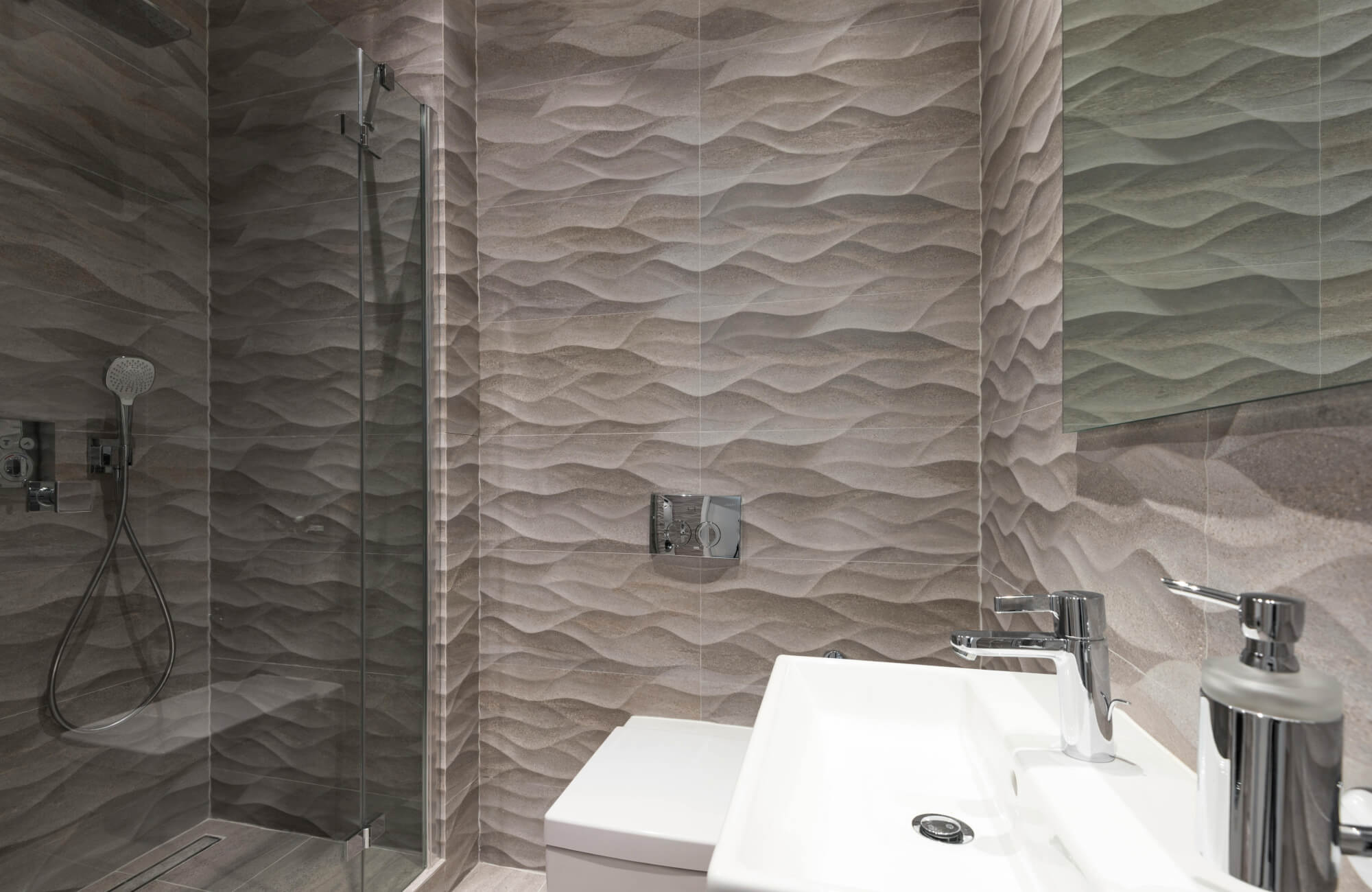 Modern bathroom featuring textured wave-patterned wall tiles in neutral tones, a sleek glass-enclosed shower, and contemporary chrome fixtures.
