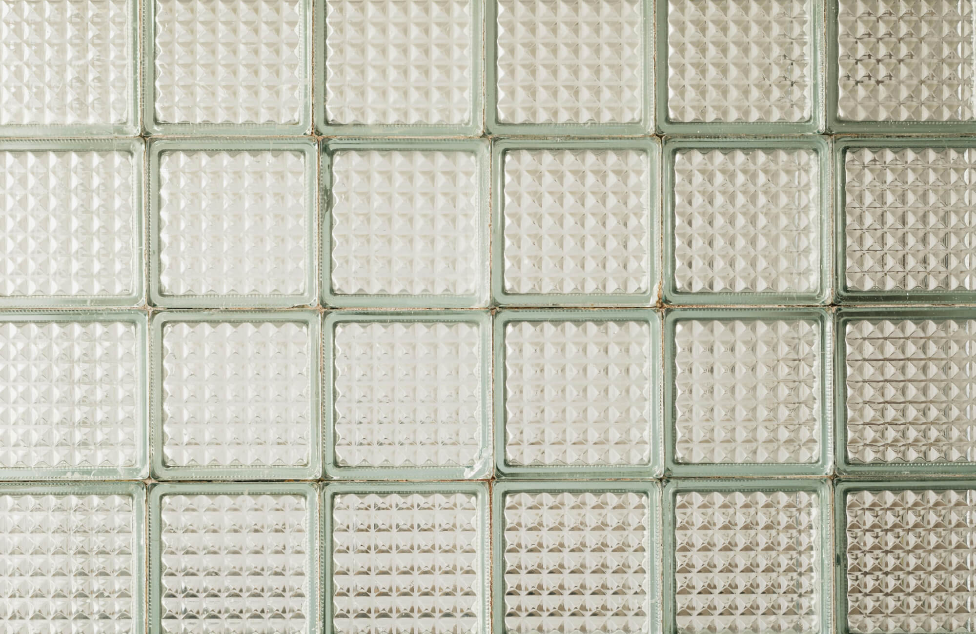 Close-up of textured glass block shower tiles with a geometric pattern, framed by subtle green-tinted edges for a retro yet modern aesthetic.