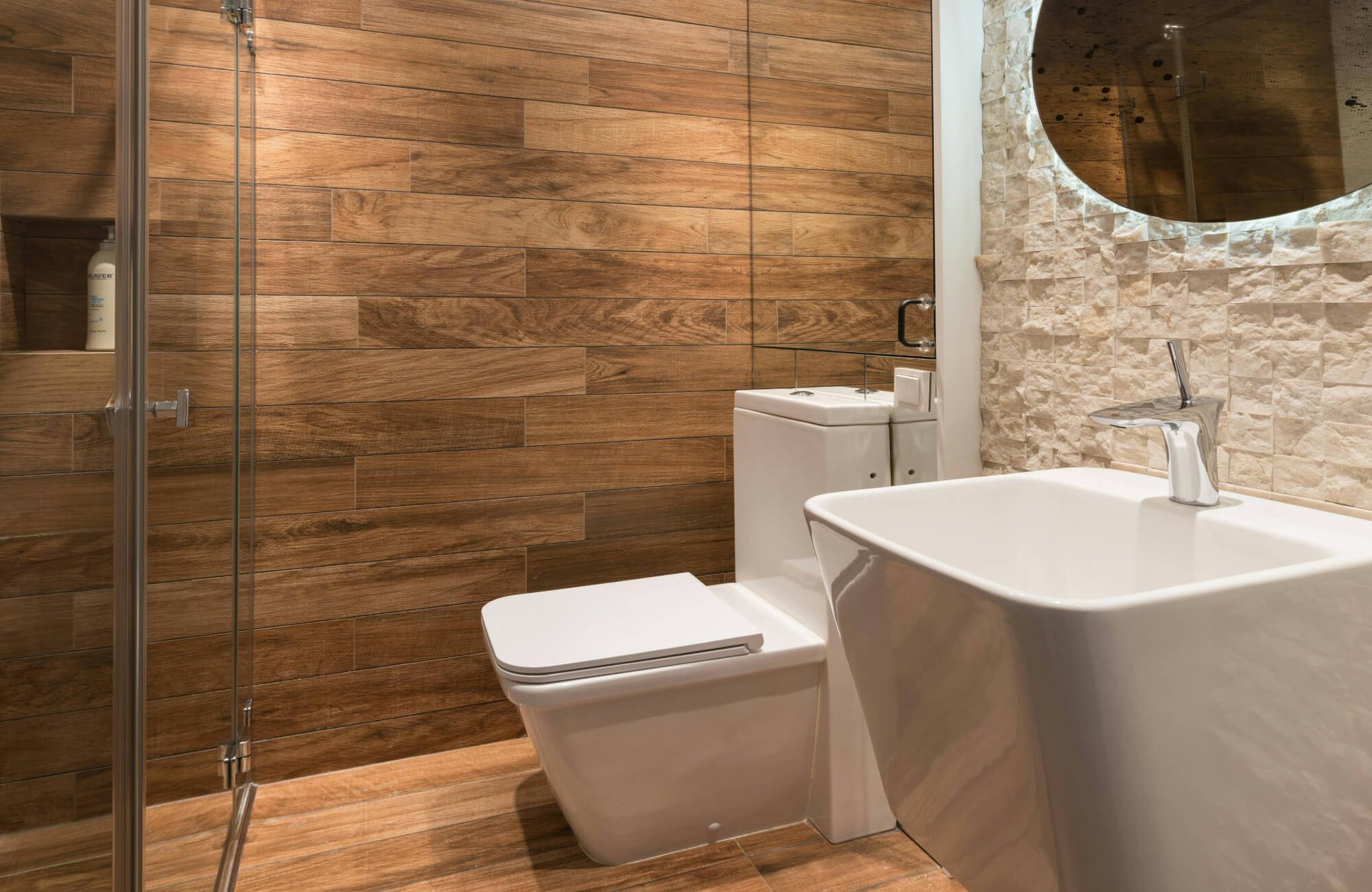 Modern bathroom featuring wood tiles on the walls and floor, paired with textured stone accents and sleek white fixtures.