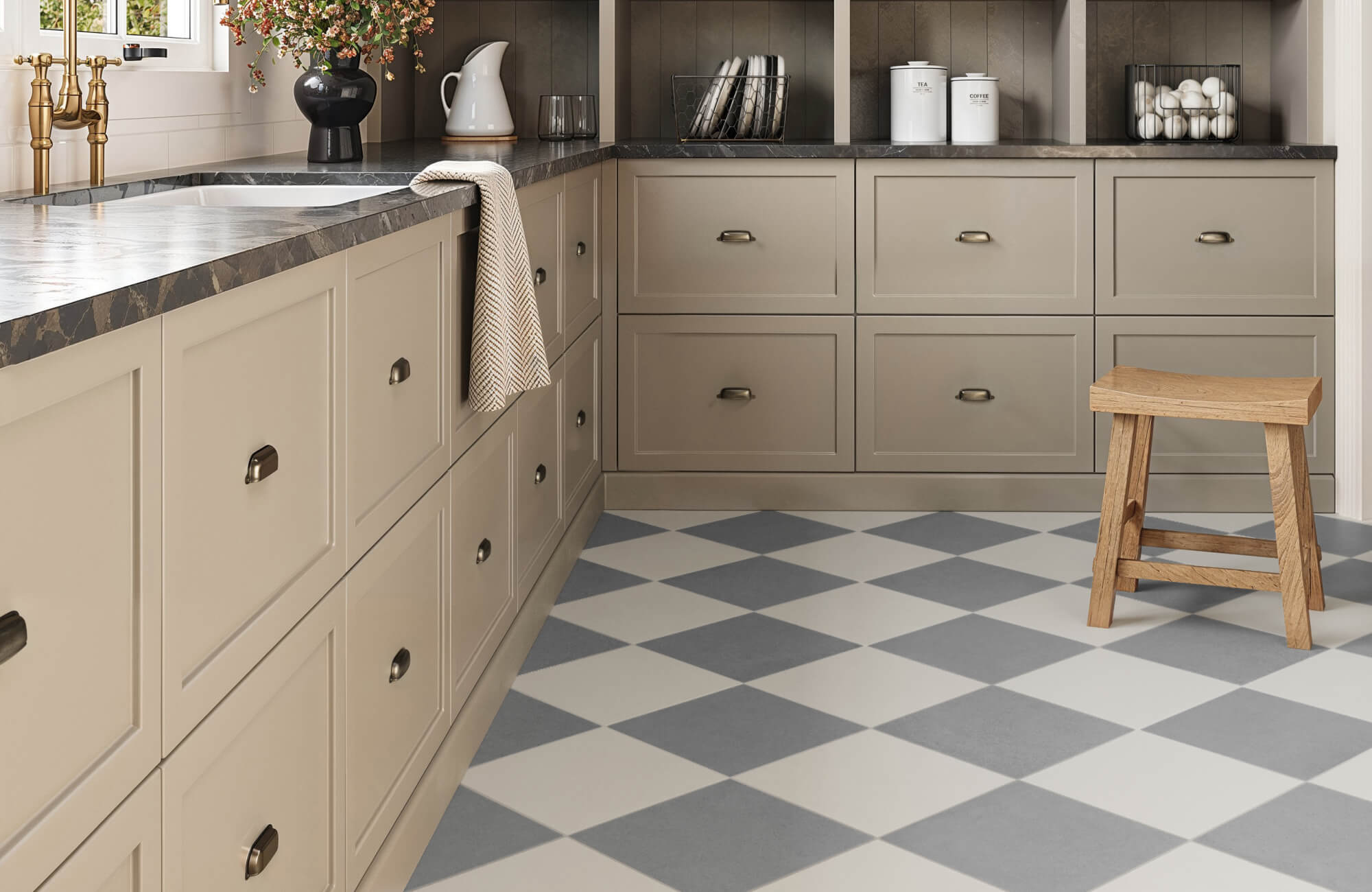Cozy kitchen with a diagonal checkerboard floor, taupe cabinetry, black stone countertops, gold fixtures, and a wooden stool for warmth.