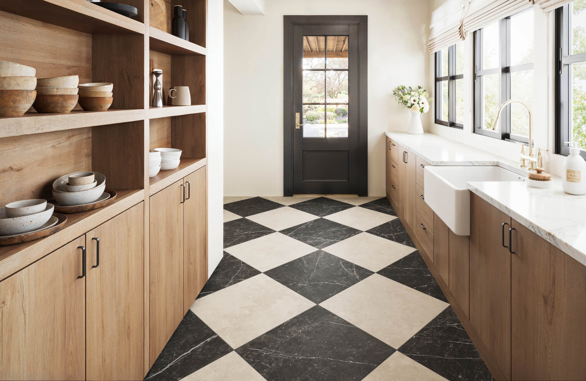 Bright and inviting kitchen with a diagonal checkerboard floor, natural wood cabinetry, open shelving, marble countertops, and black-framed windows.