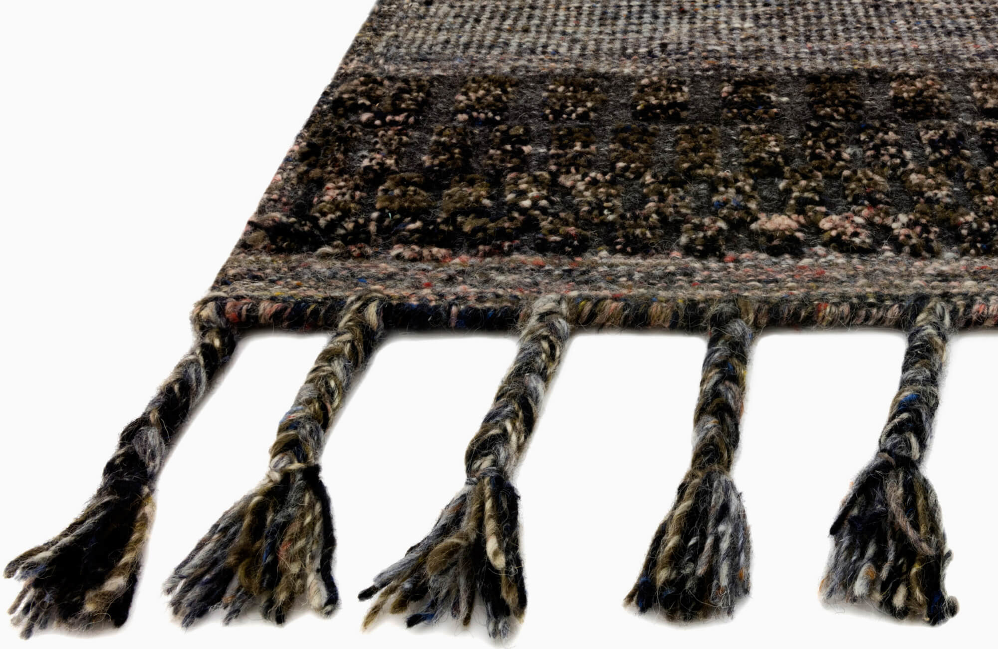 Close-up of dark woven rug with braided tassels, mixed yarn colors, and textured edge detail against a clean white background.