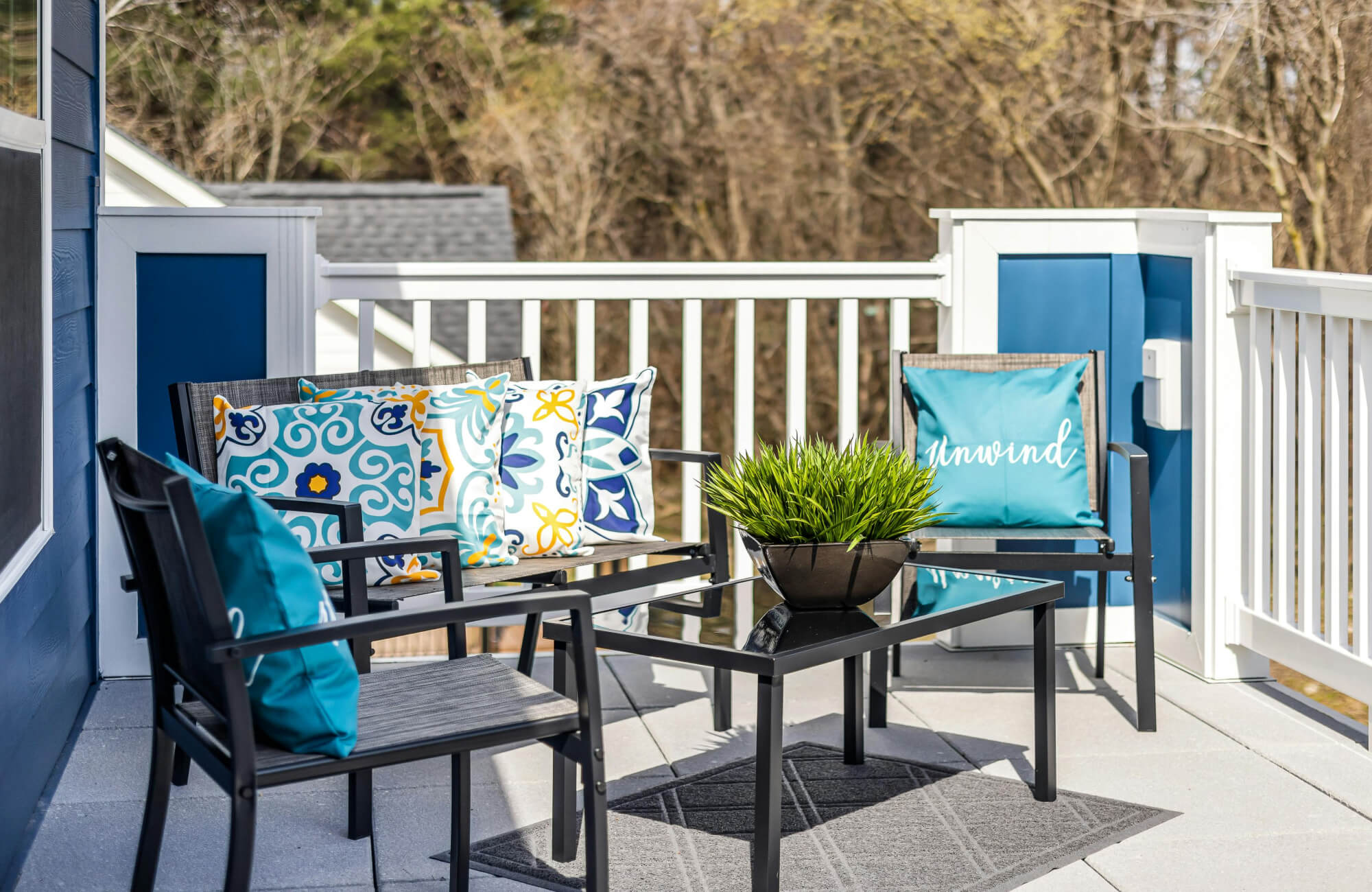 Small polypropylene outdoor rug beneath a coffee table on a balcony seating area with bright accent pillows.
