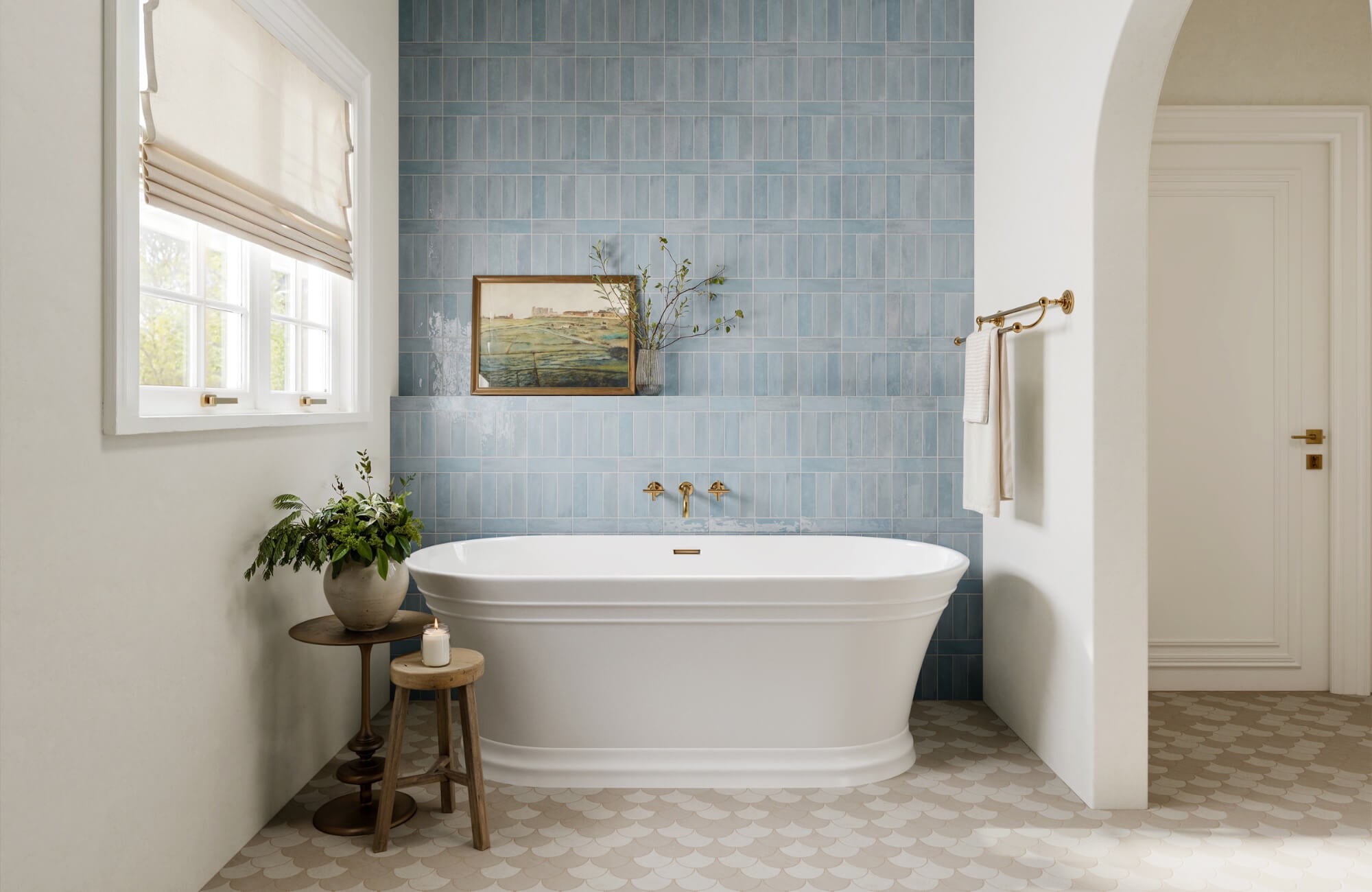 null Bright bathroom with blue wall tiles, scalloped floor tiles, freestanding tub, and brass fixtures.