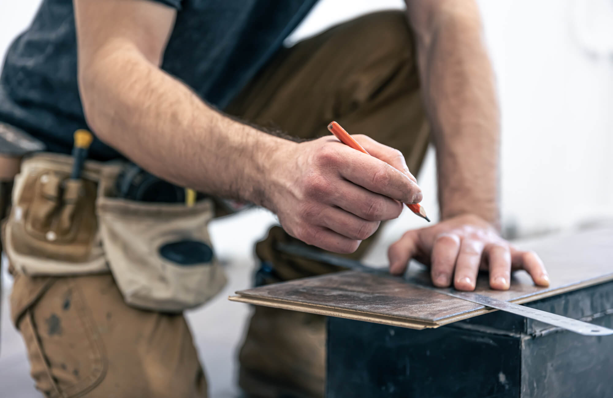 null Installer measuring and marking wood flooring plank for cutting during kitchen floor installation with carpenter tools and workbench.