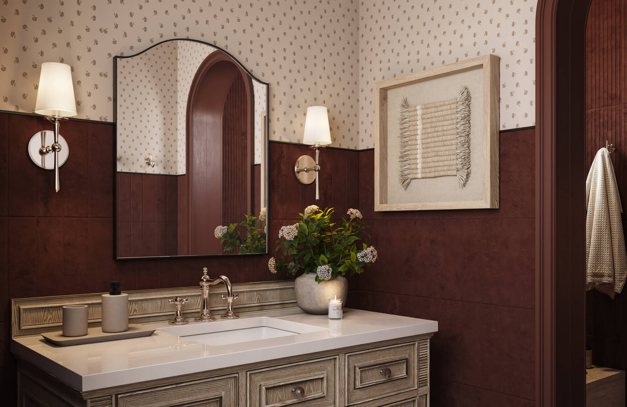 Traditional bathroom with patterned wallpaper, dark red wood wall paneling, framed woven textile wall art above a rustic wood vanity, and an arched mirror with brass sconces.