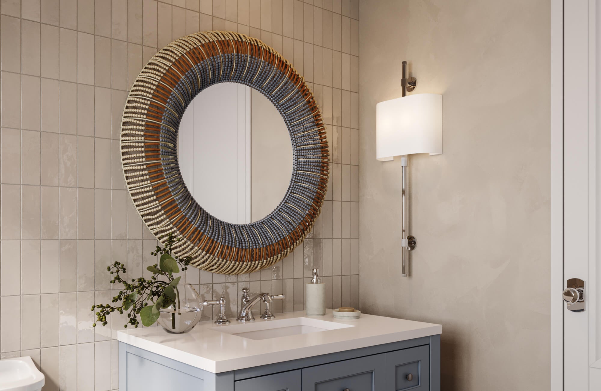 Small bathroom vanity area with glossy tiled walls, a sculptural woven round mirror above a light blue vanity, chrome fixtures, and soft neutral finishes.