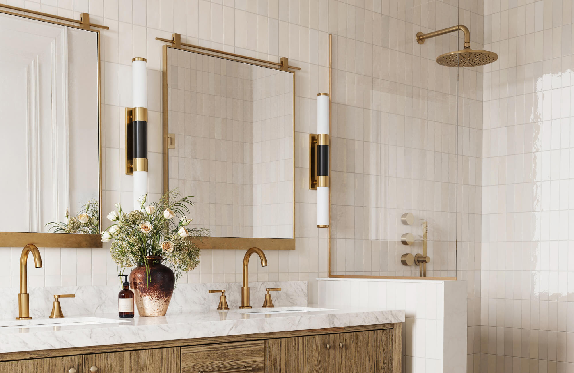 Bathroom with dual square brass-framed mirrors, marble countertop, wood vanity, modern sconces, and a walk-in shower with brass fixtures.