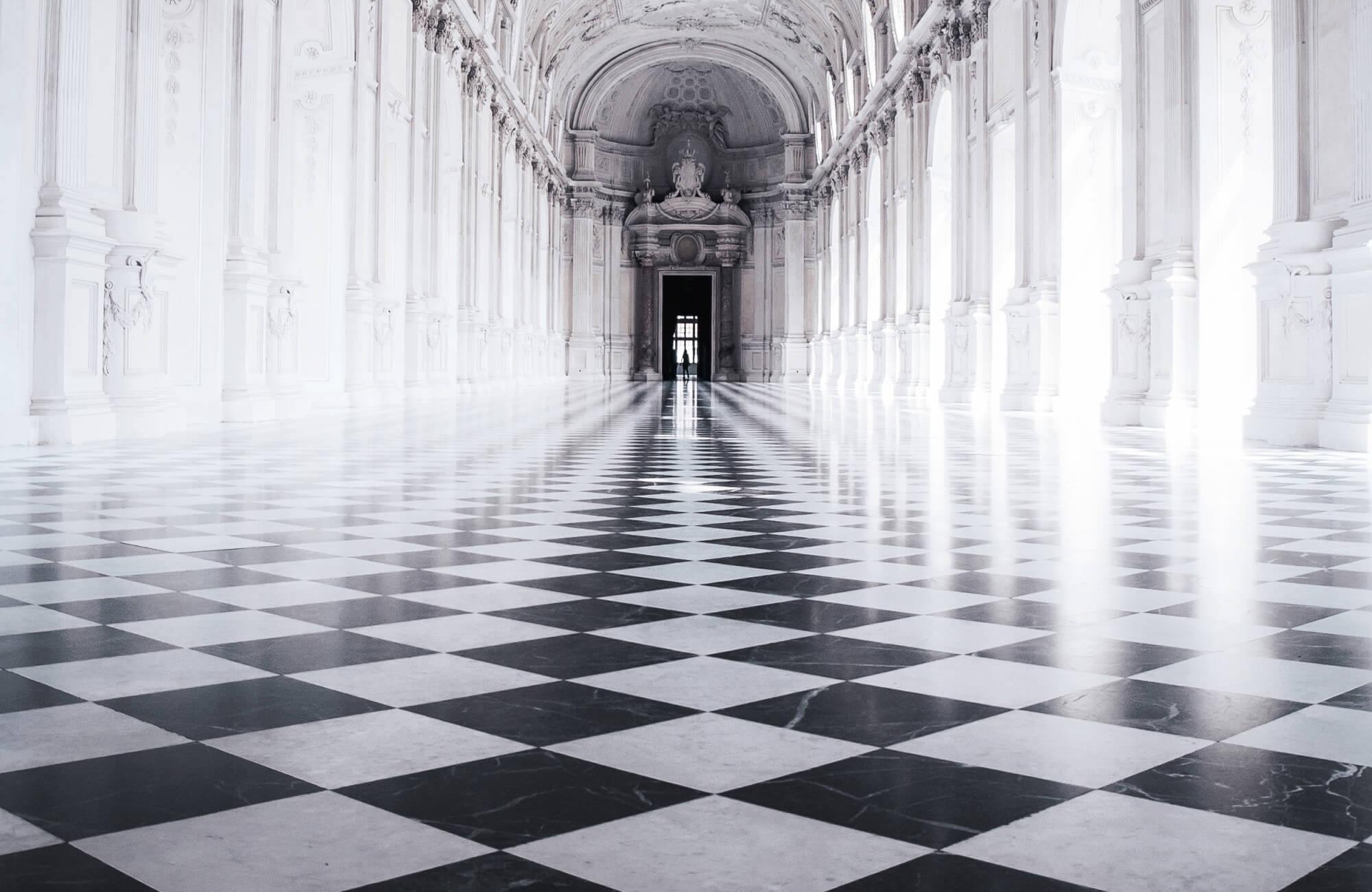 A breathtaking palace hall featuring a grand black-and-white checkerboard marble floor, ornate Baroque architecture, and towering arched windows.