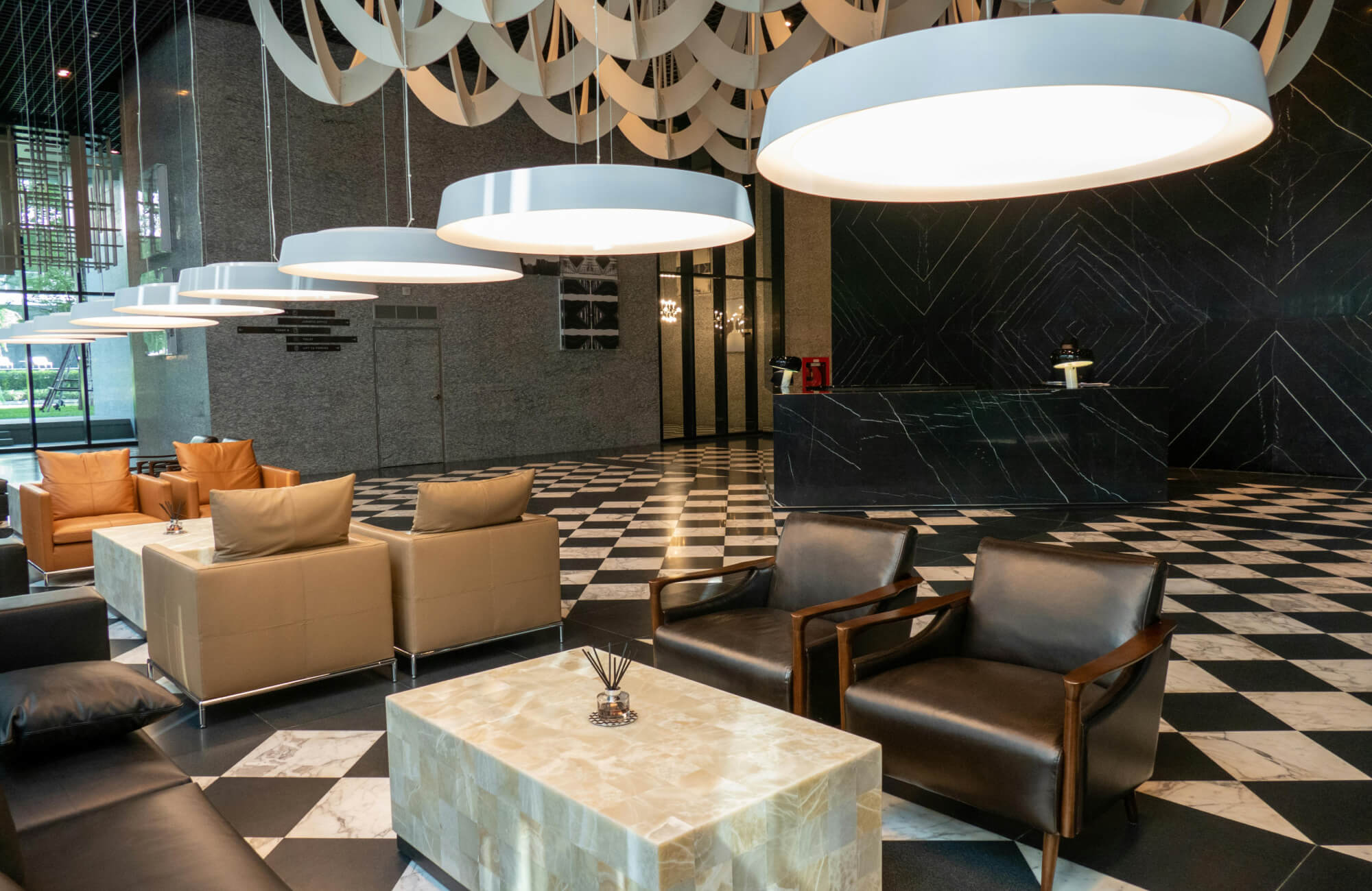 A hotel lobby with Art Deco influences, featuring a bold black and white checkerboard floor, sleek leather seating, and oversized pendant lights.