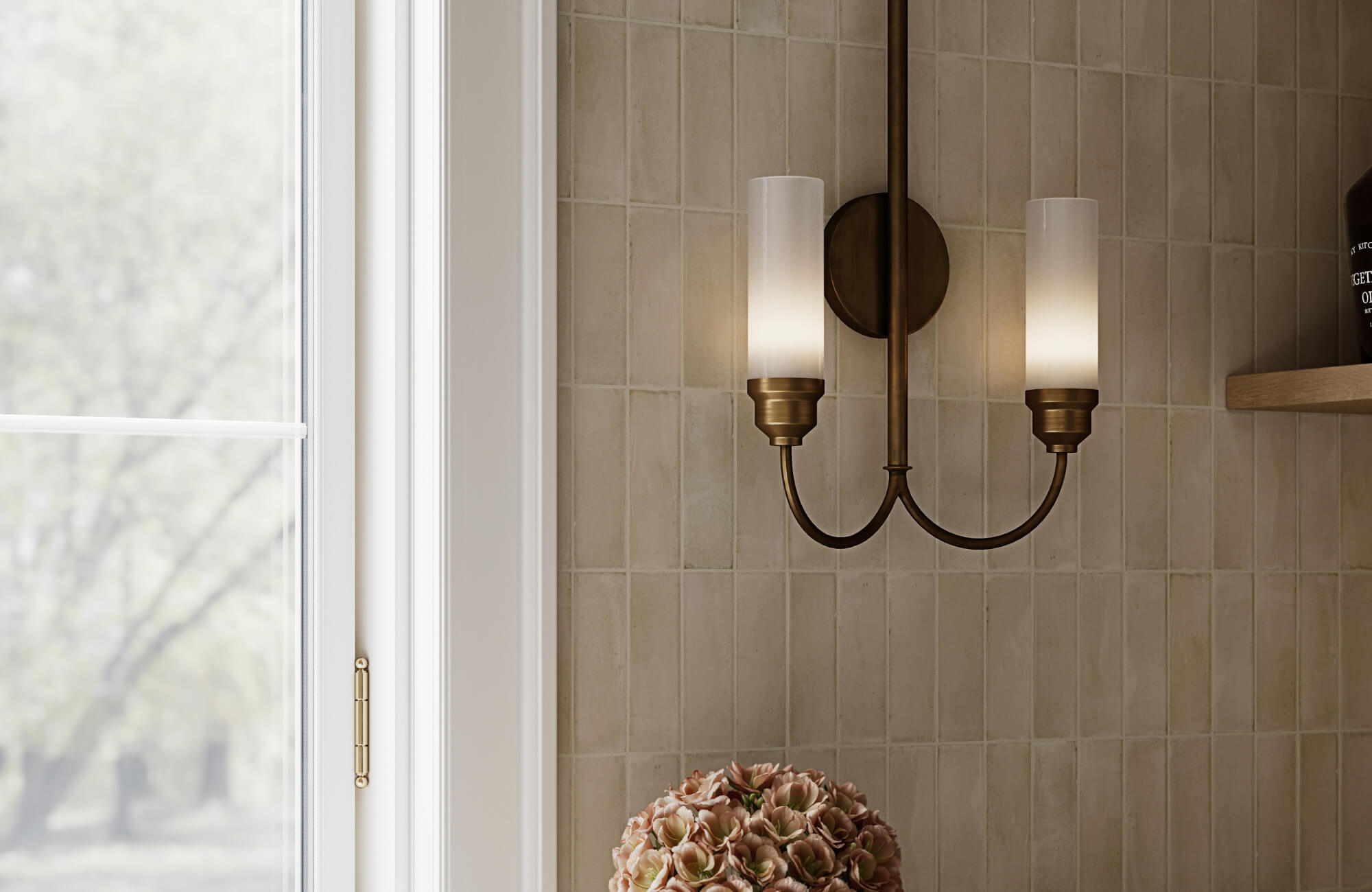 Elegant double-arm wall sconce with frosted cylindrical shades and bronze finish mounted on tiled wall beside a window and flowers.
