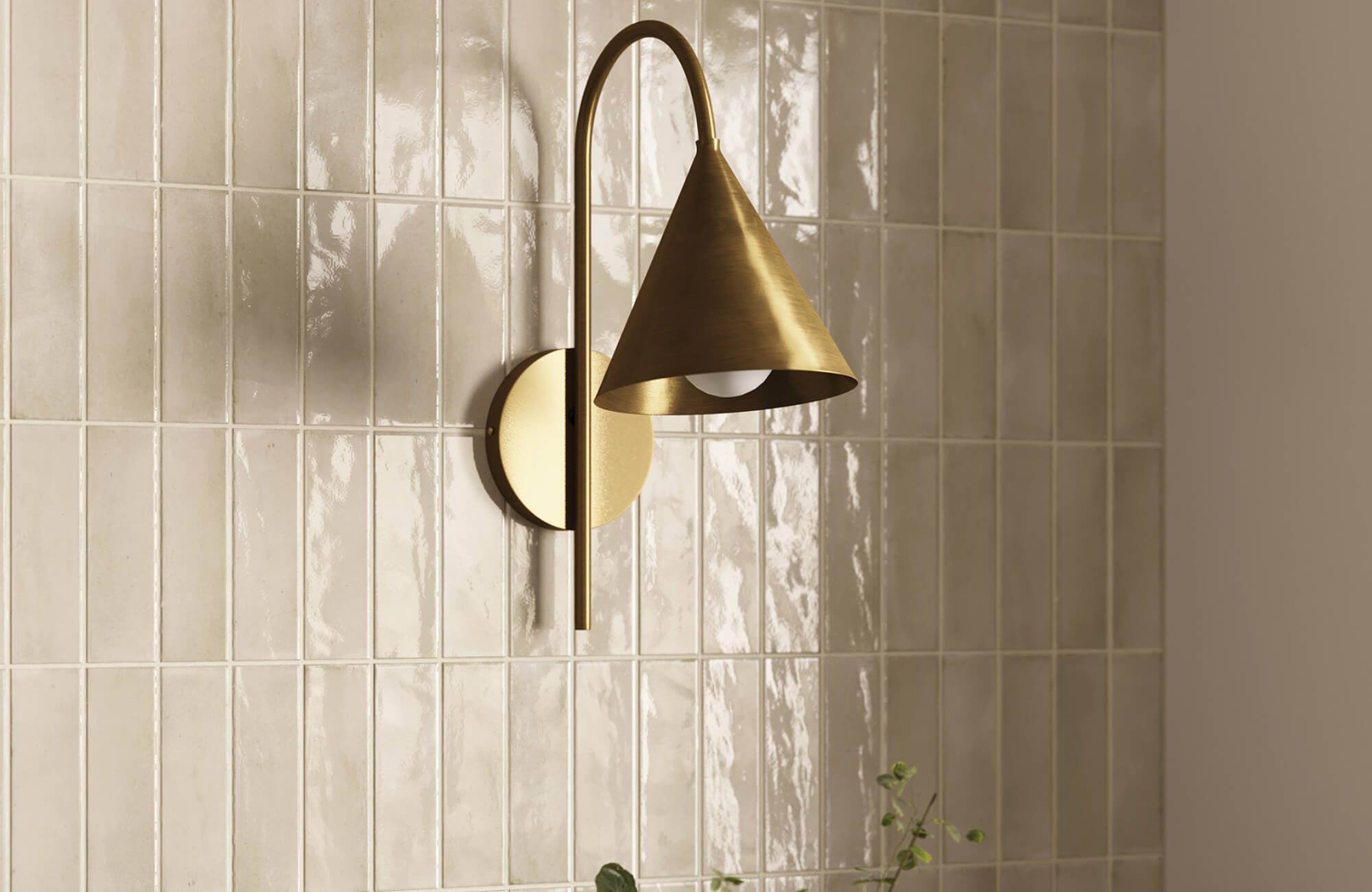 Modern brass wall sconce with a conical shade and curved arm mounted on glossy beige tiled wall, casting focused downward light.