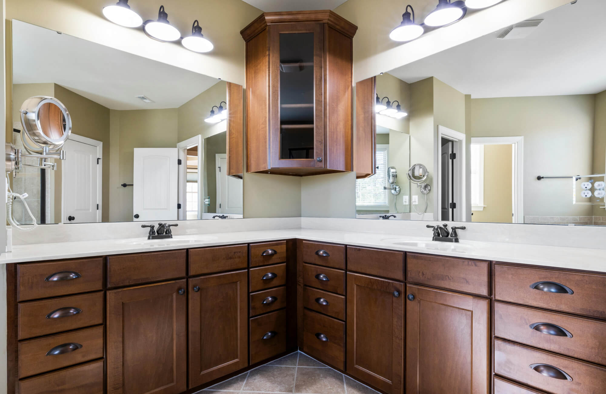 A corner vanity bathroom with dark wood cabinetry, dual sinks, and wraparound mirrors, showing how a corner layout can support storage and symmetry in a shared bathroom.