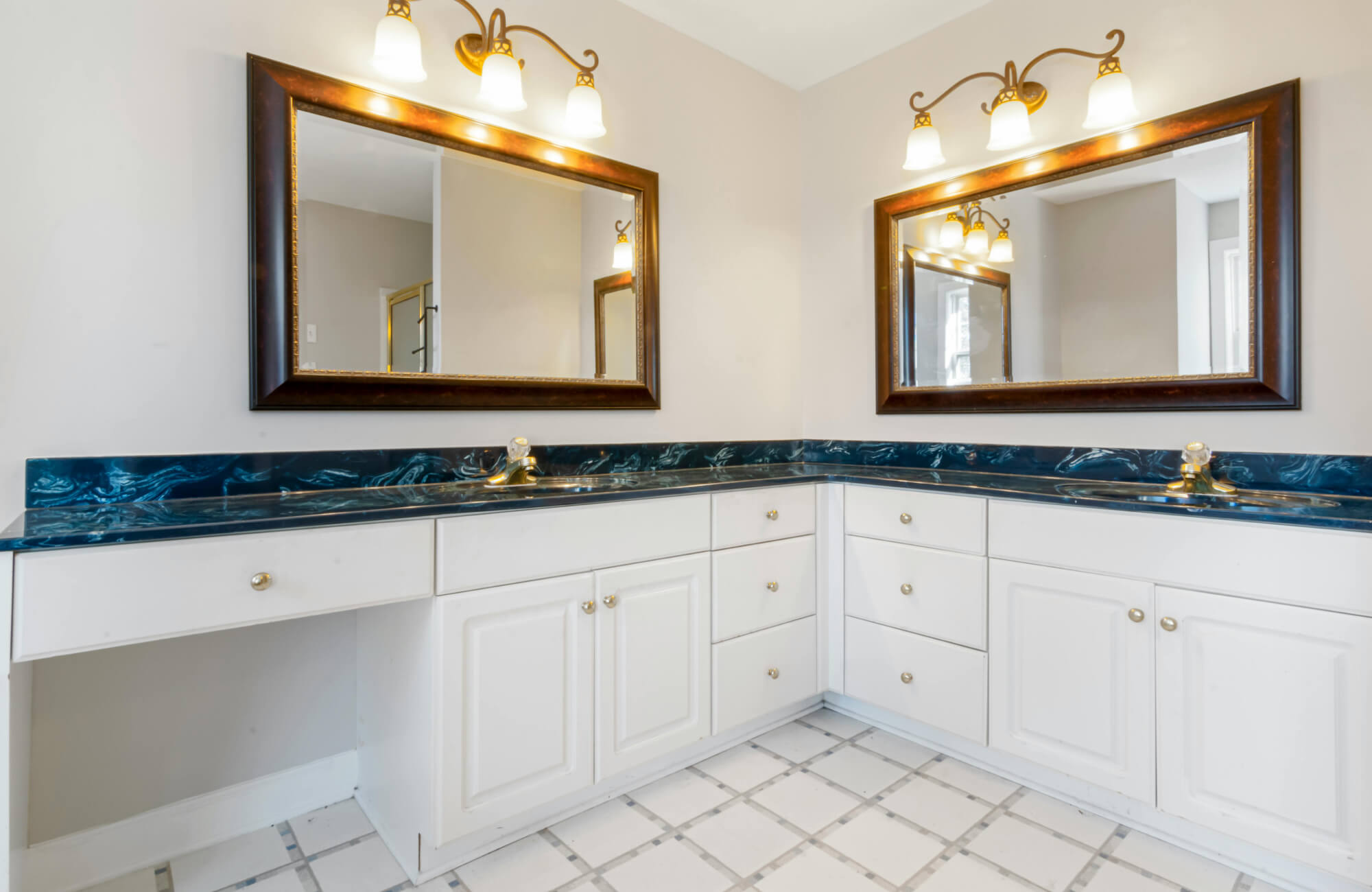 A corner vanity layout with integrated drawers, double mirrors, and wall-mounted lighting, illustrating a practical solution for bathrooms that need more surface area in limited space.