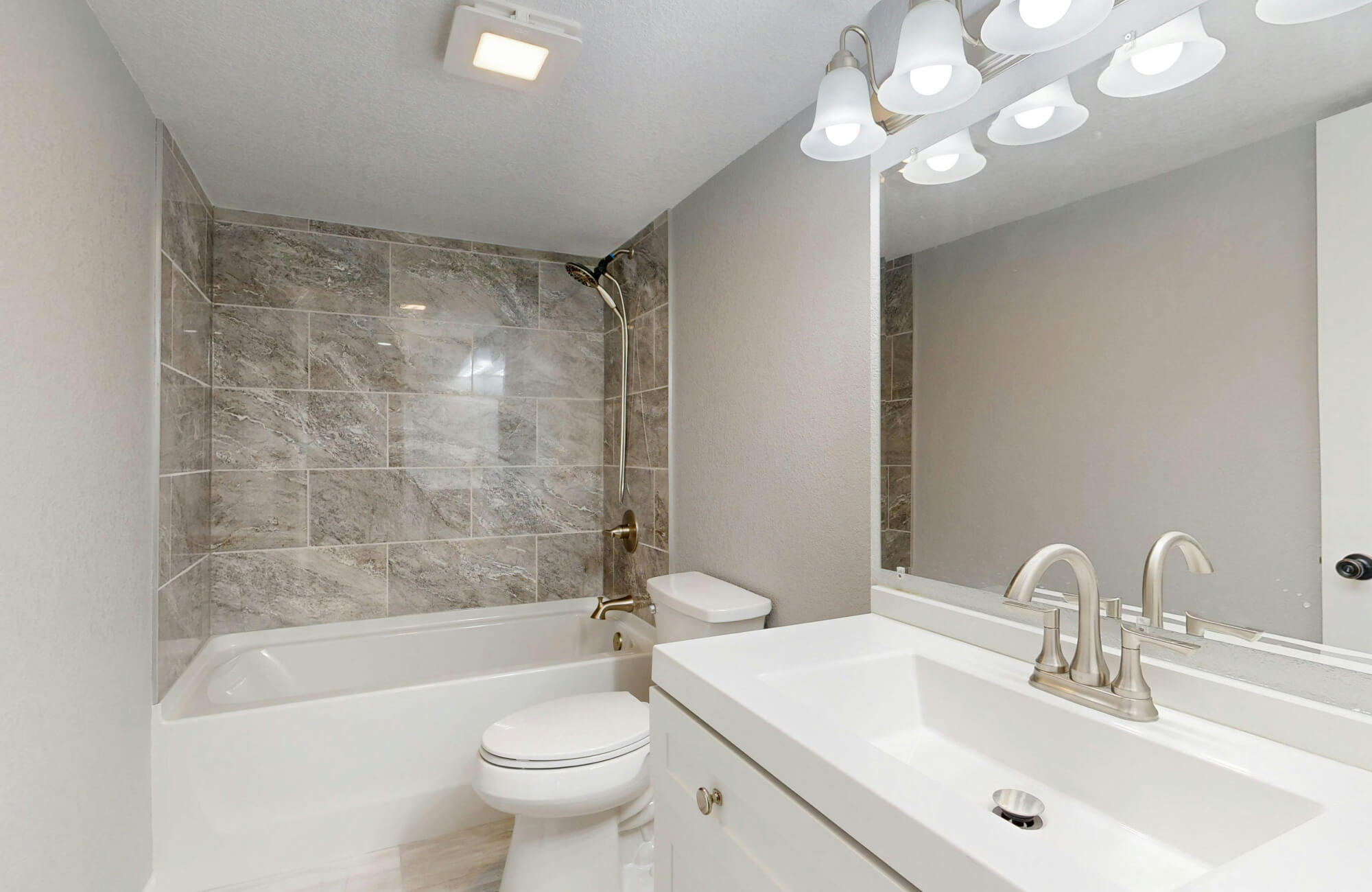 A compact bathroom with a standard vanity placed beside a tub-shower combo, showing a layout where wall space is prioritized over a corner vanity.