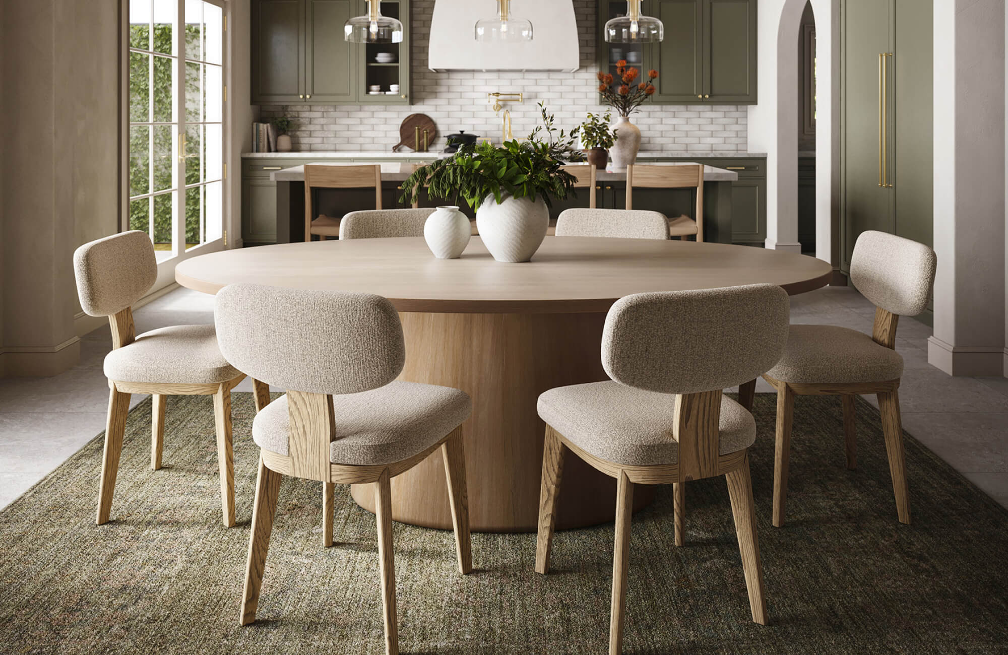 A round dining table is placed fully on a rug in an open layout, clearly separating the dining area from the kitchen