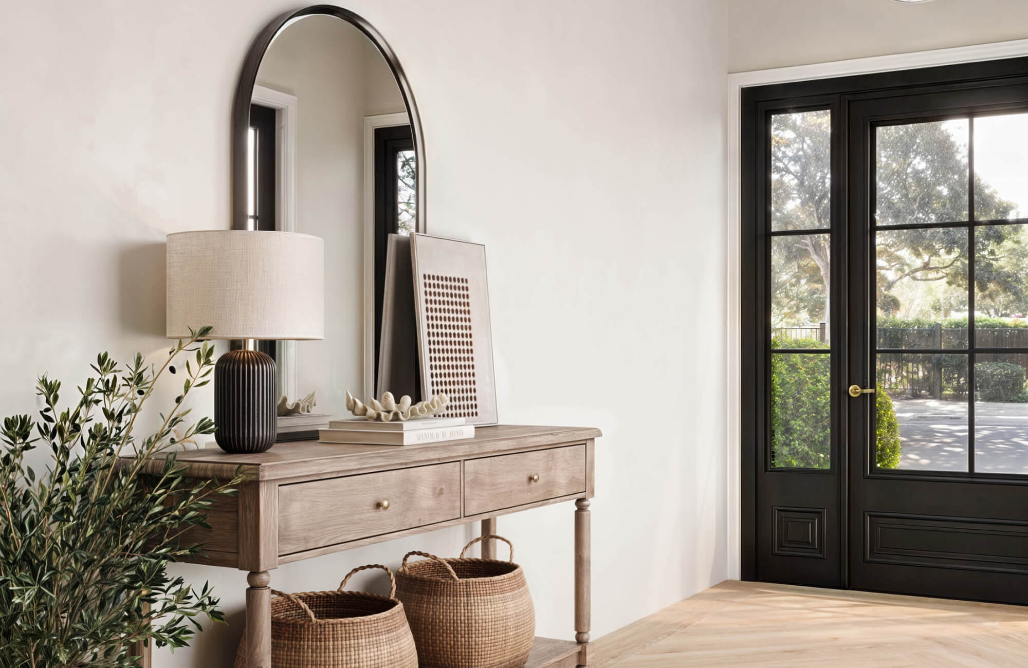 Tall arch mirror placed above entry console near black framed glass doors