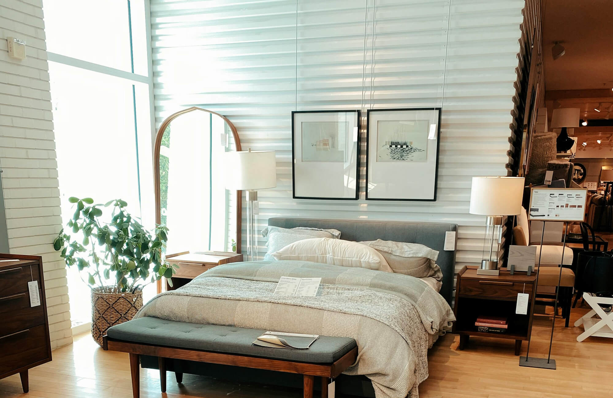 Leaning arch mirror beside bed near large window, reflecting soft natural light